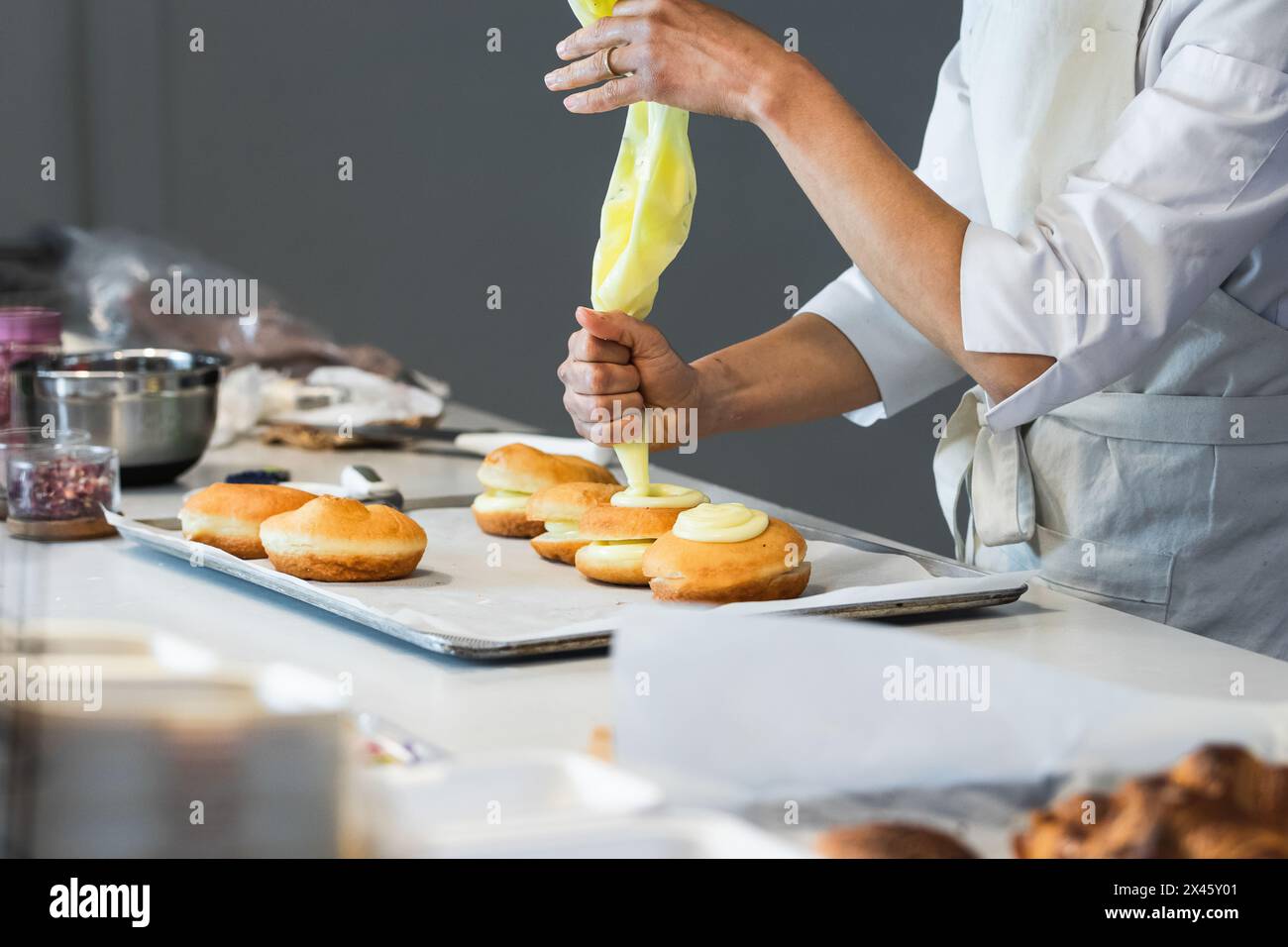 Vista laterale del panettiere anonimo raccolto spremitura crema da sacchetto di pasticceria mentre decorando dolce vegan berliners in cucina in panetteria Foto Stock