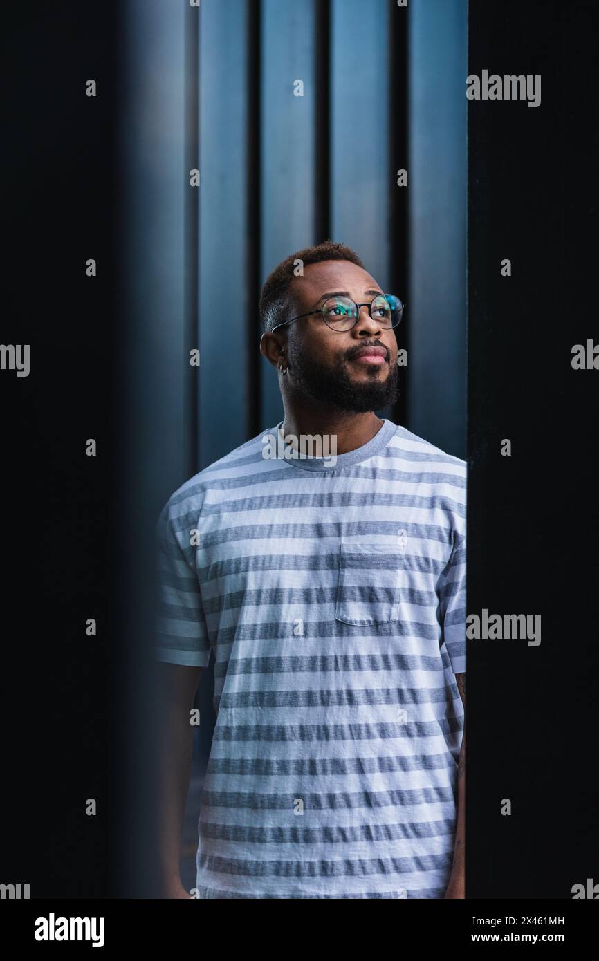 Uomo afroamericano positivo sicuro con barba e bicchieri indossare una camicia a righe casual che si affaccia sullo sfondo sfocato Foto Stock