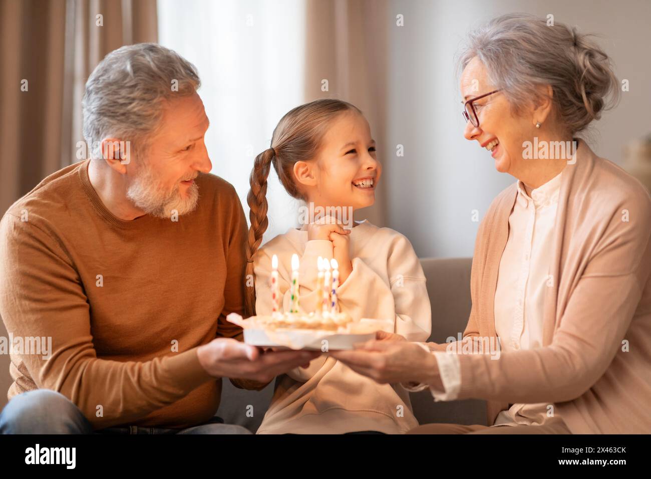 Smiling Girl celebra il compleanno con i nonni in una casa accogliente Foto Stock
