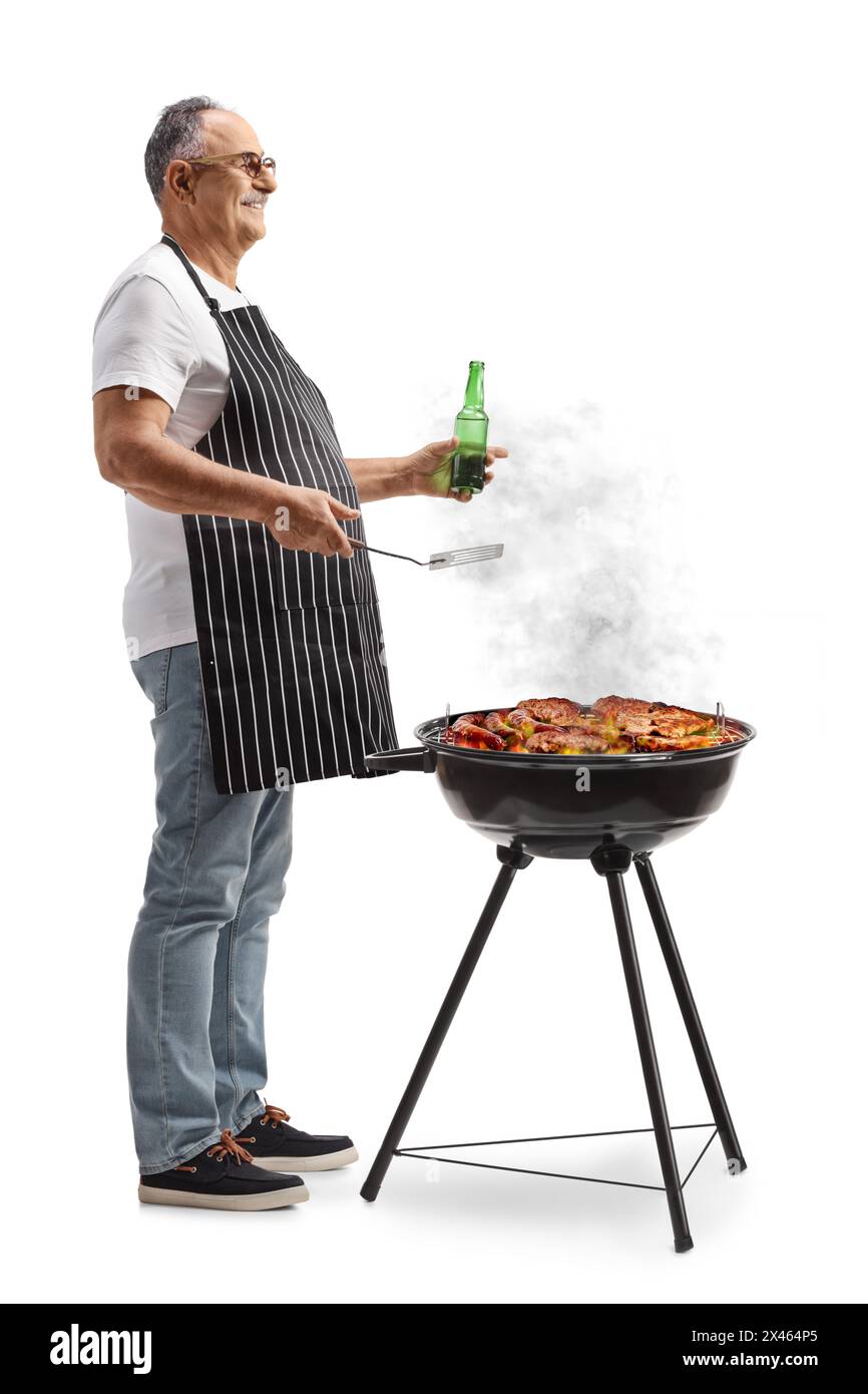 Uomo maturo che indossa un grembiule con una bottiglia di birra e carne alla griglia su un barbecue isolato su sfondo bianco Foto Stock