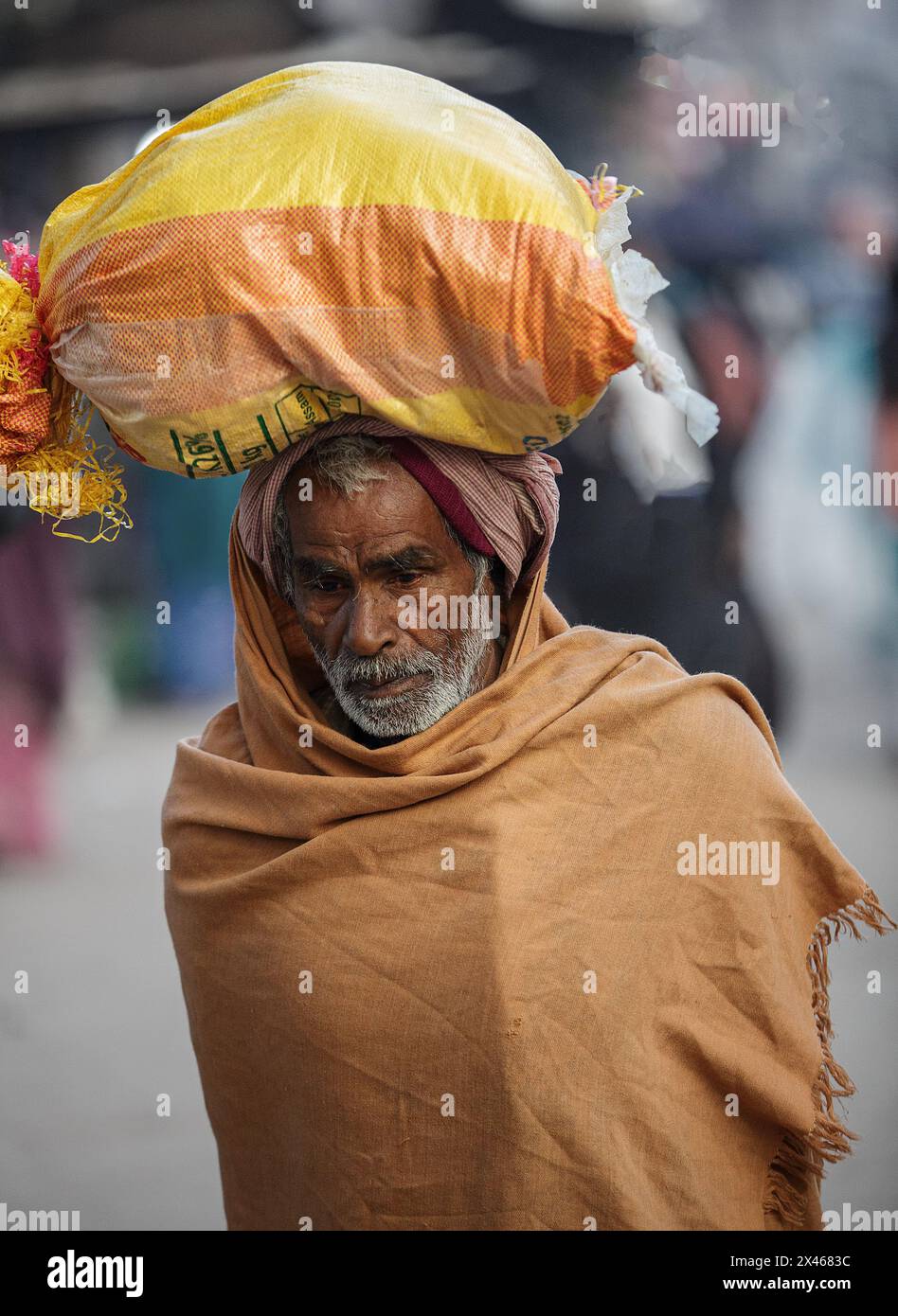 Pellegrino che cammina con gli effetti personali in un sacco sulla testa a Varanasi, in India. Foto Stock
