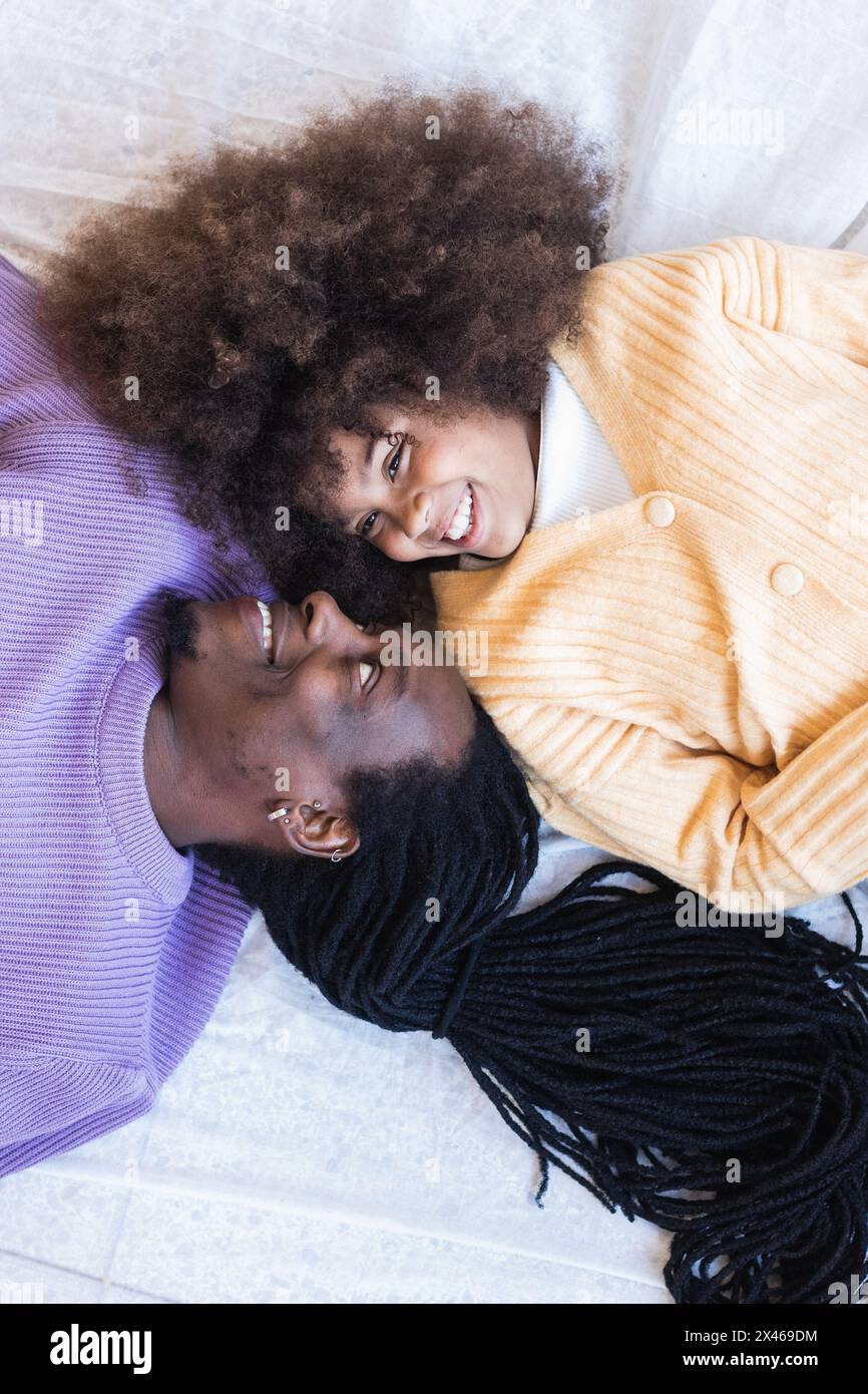Vista dall'alto di sorridente padre afroamericano mentito con adorabile piccola figlia mentre trascorrono il fine settimana insieme Foto Stock