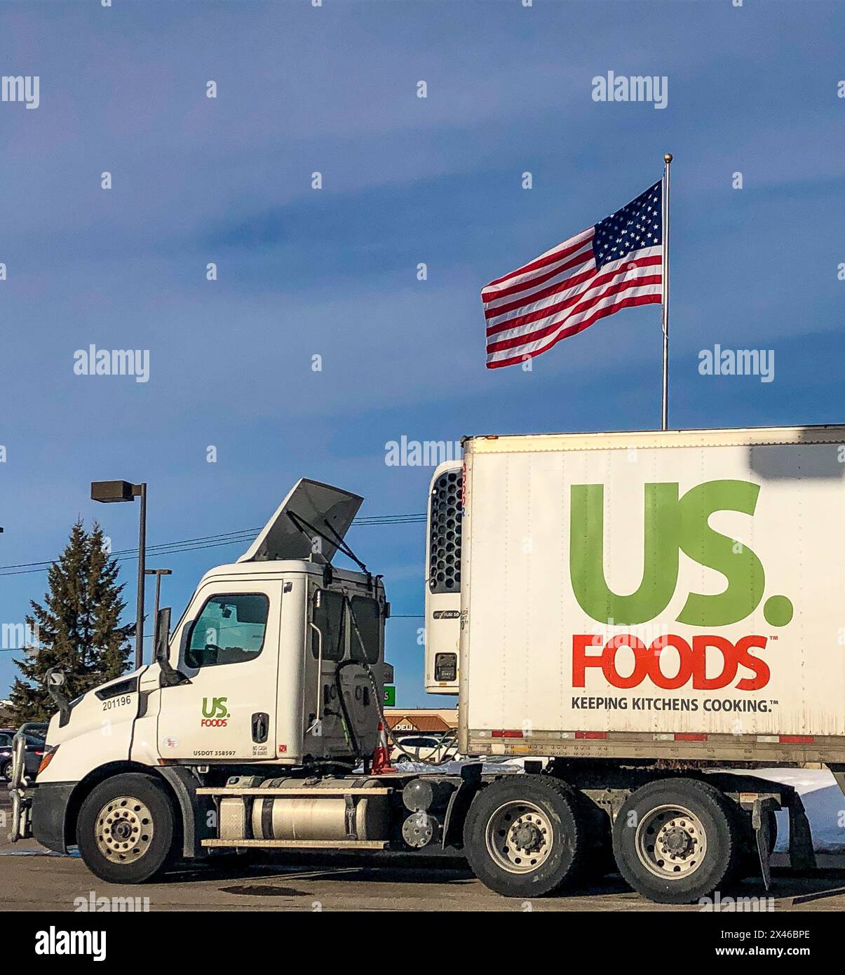 Semi-camion che trasporta merci per US Foods su strada, con una bandiera americana sullo sfondo vista sopra il rimorchio. Foto Stock