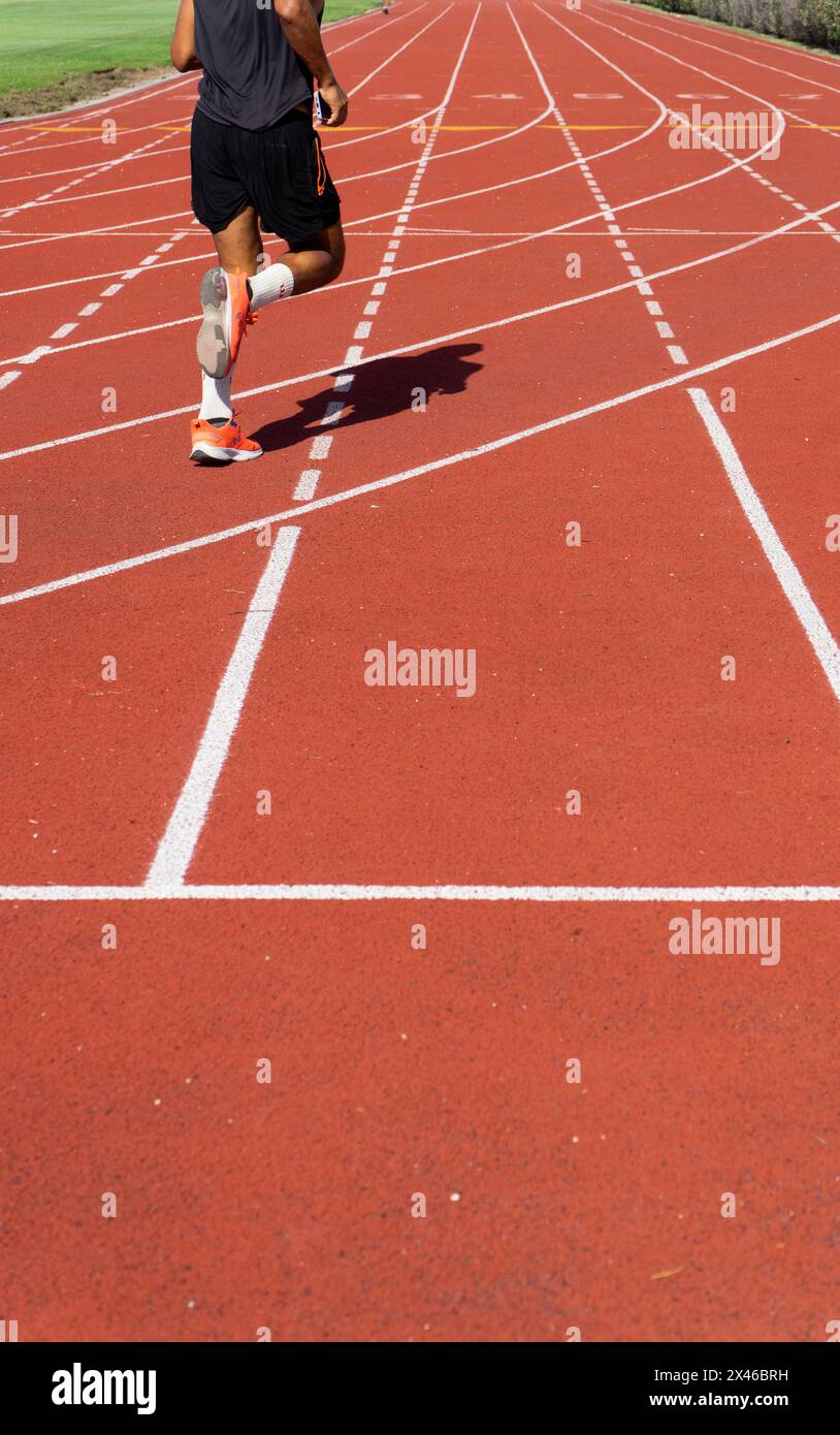 L'atleta si allena sulla pista rossa di atletica, che mette in risalto la velocità e l'agilità dell'uomo ritratto da dietro, in un centro sportivo all'aperto a Par Foto Stock