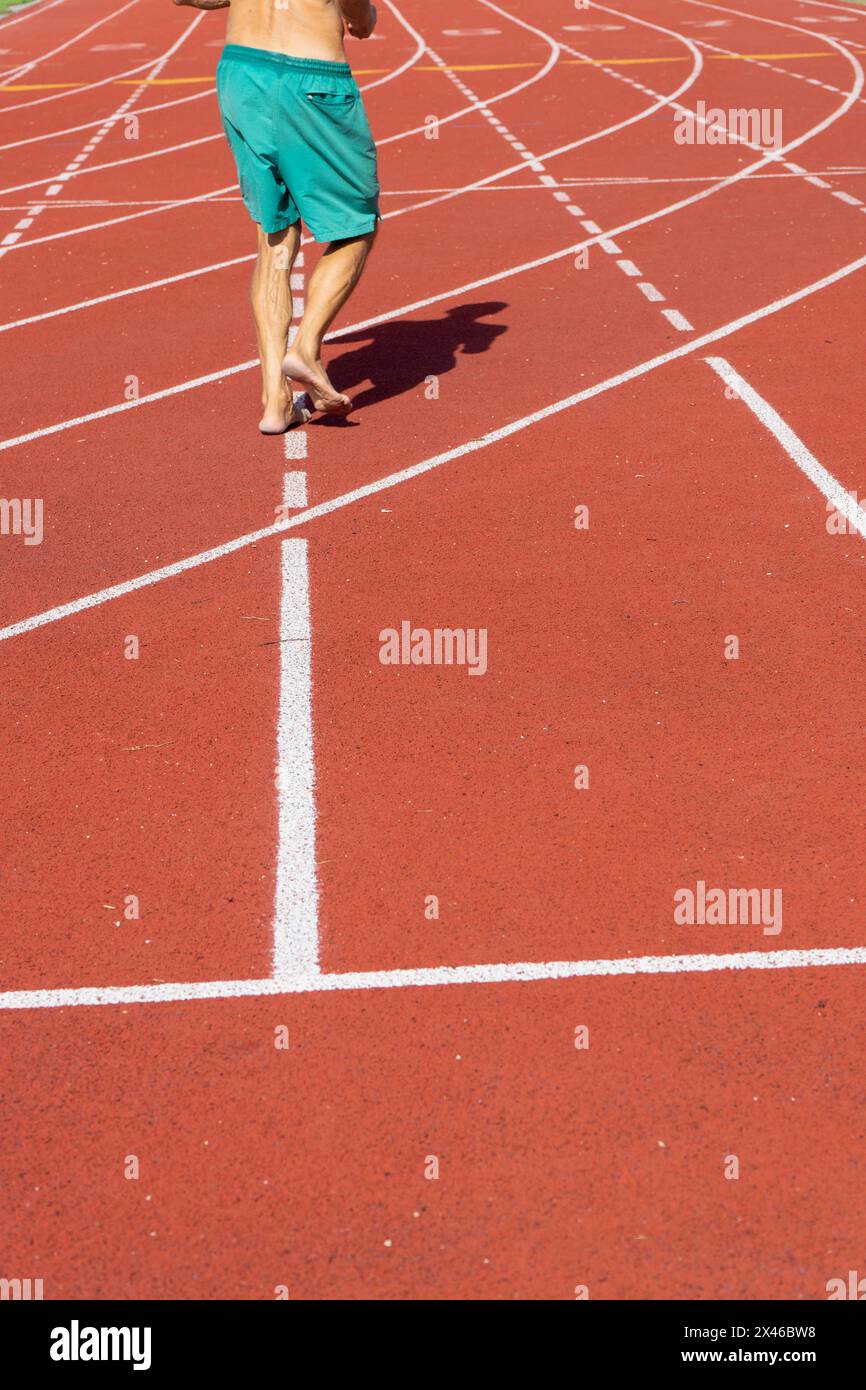 Un atleta senior cammina a piedi nudi lungo la pista di allenamento in un centro di atletica a Parigi, in Francia, durante una giornata di sole con temperature elevate Foto Stock