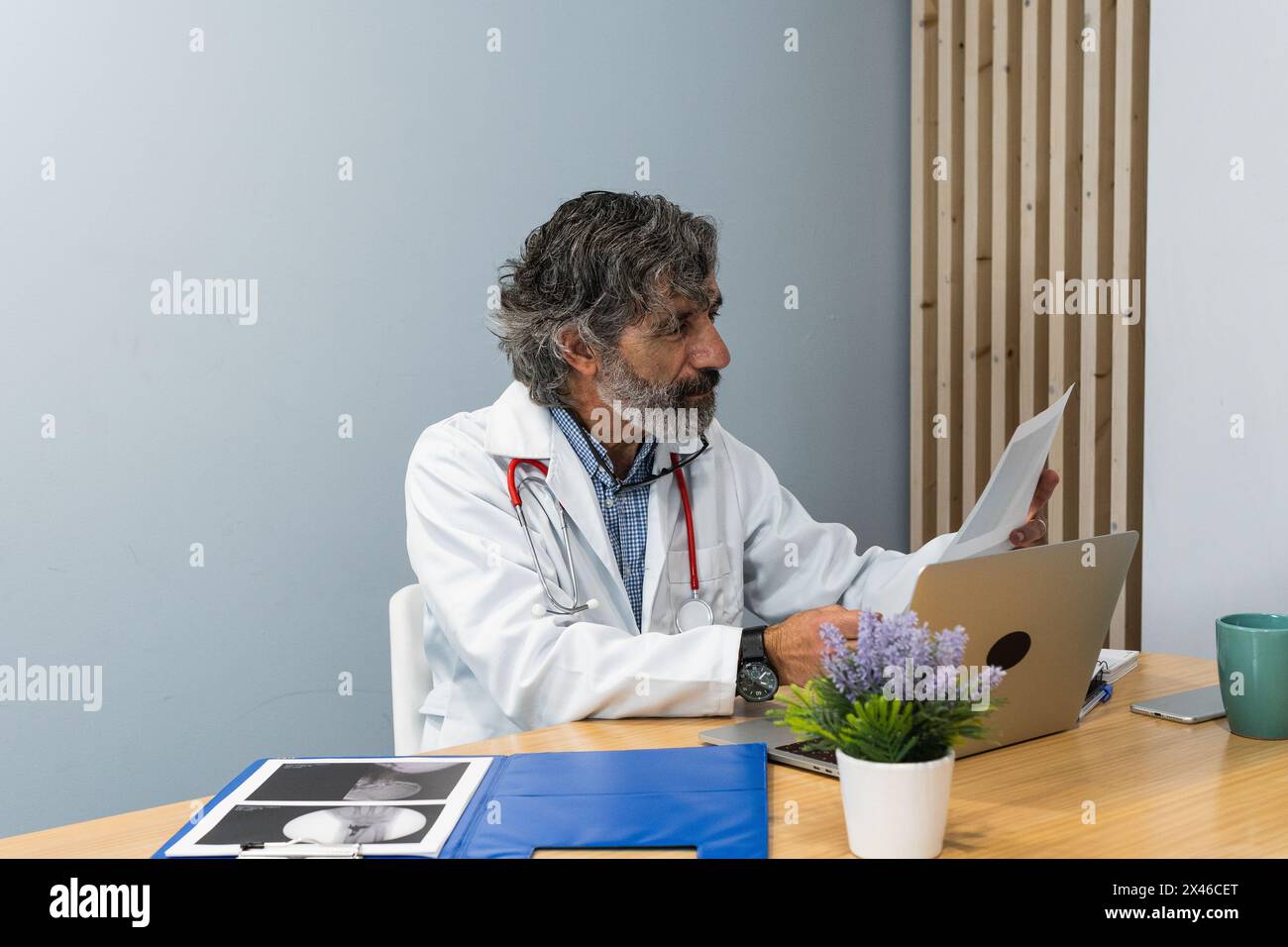 Anziano medico maschile seduto al tavolo in studio medico e l'esame dei raggi X mentre si lavora in clinica Foto Stock