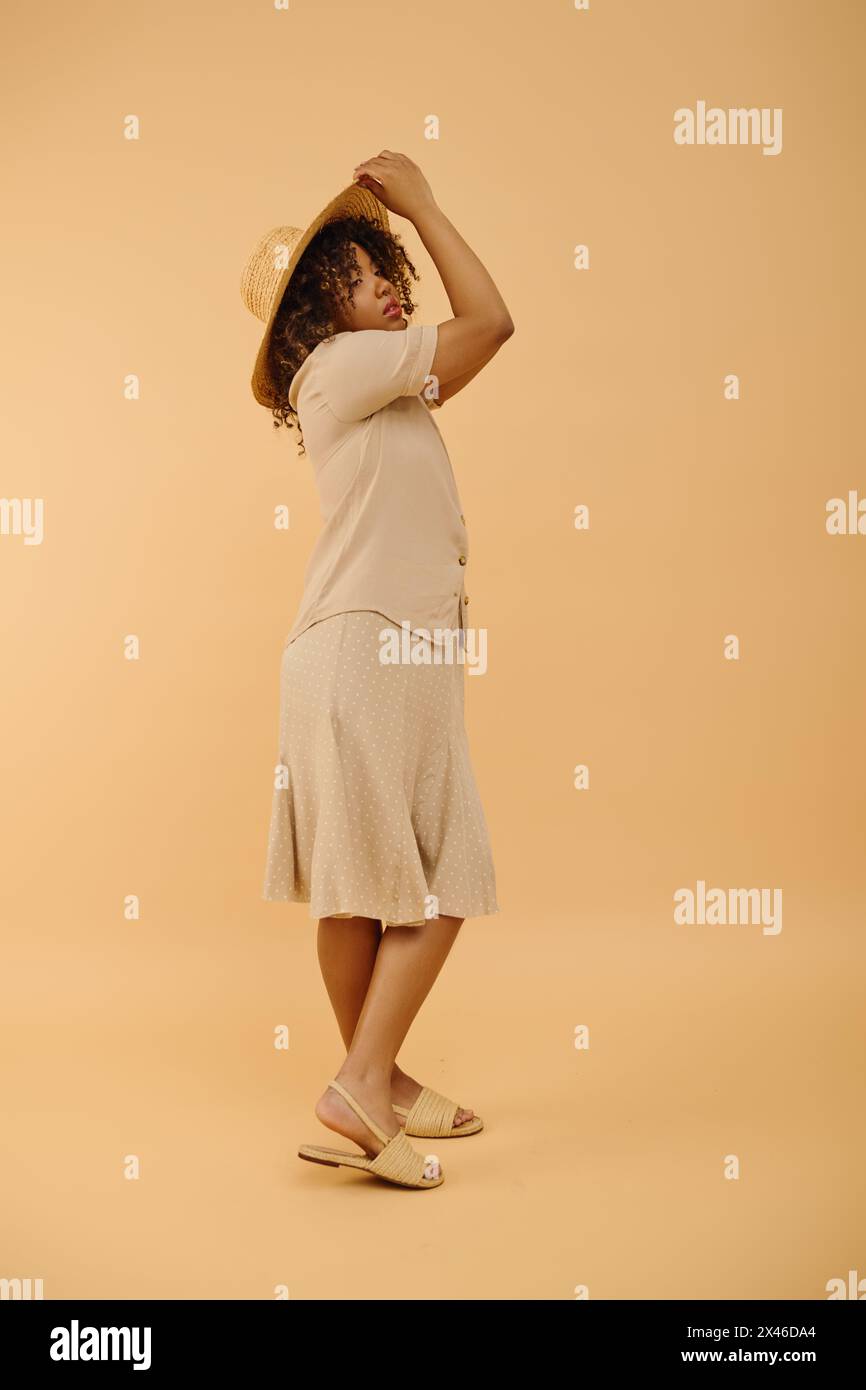 Una bella giovane donna afroamericana con capelli ricci che indossa un vestito bianco e un cappello di paglia in un ambiente da studio. Foto Stock