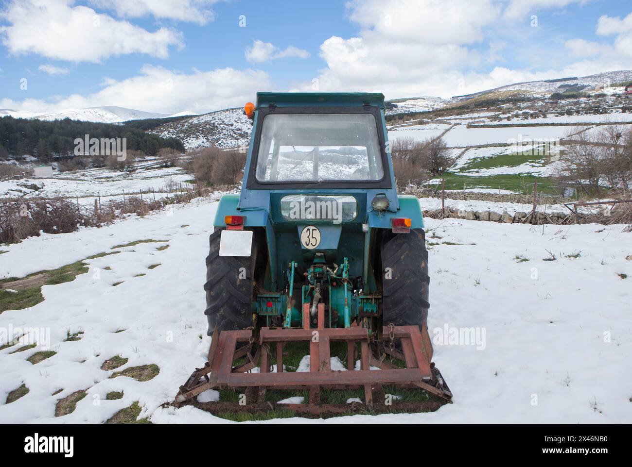 Vecchio trattore dotato di attrezzo parcheggiato in mezzo a un prato innevato. Concetto di agricoltura di montagna Foto Stock