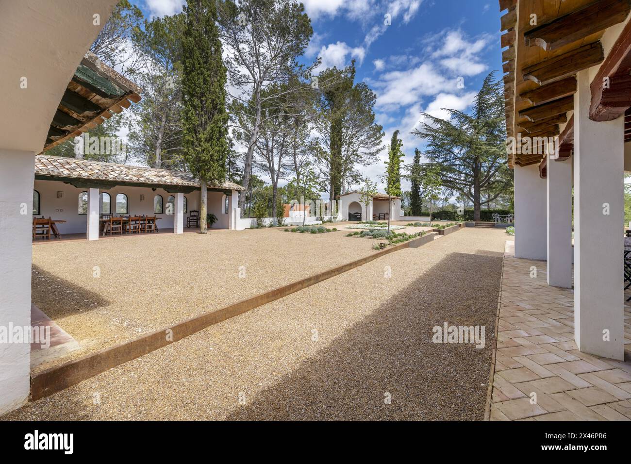 Una galleria con soffitti in legno nel patio di una casa in stile fattoria andalusa con pavimenti in ghiaia e molti alberi Foto Stock