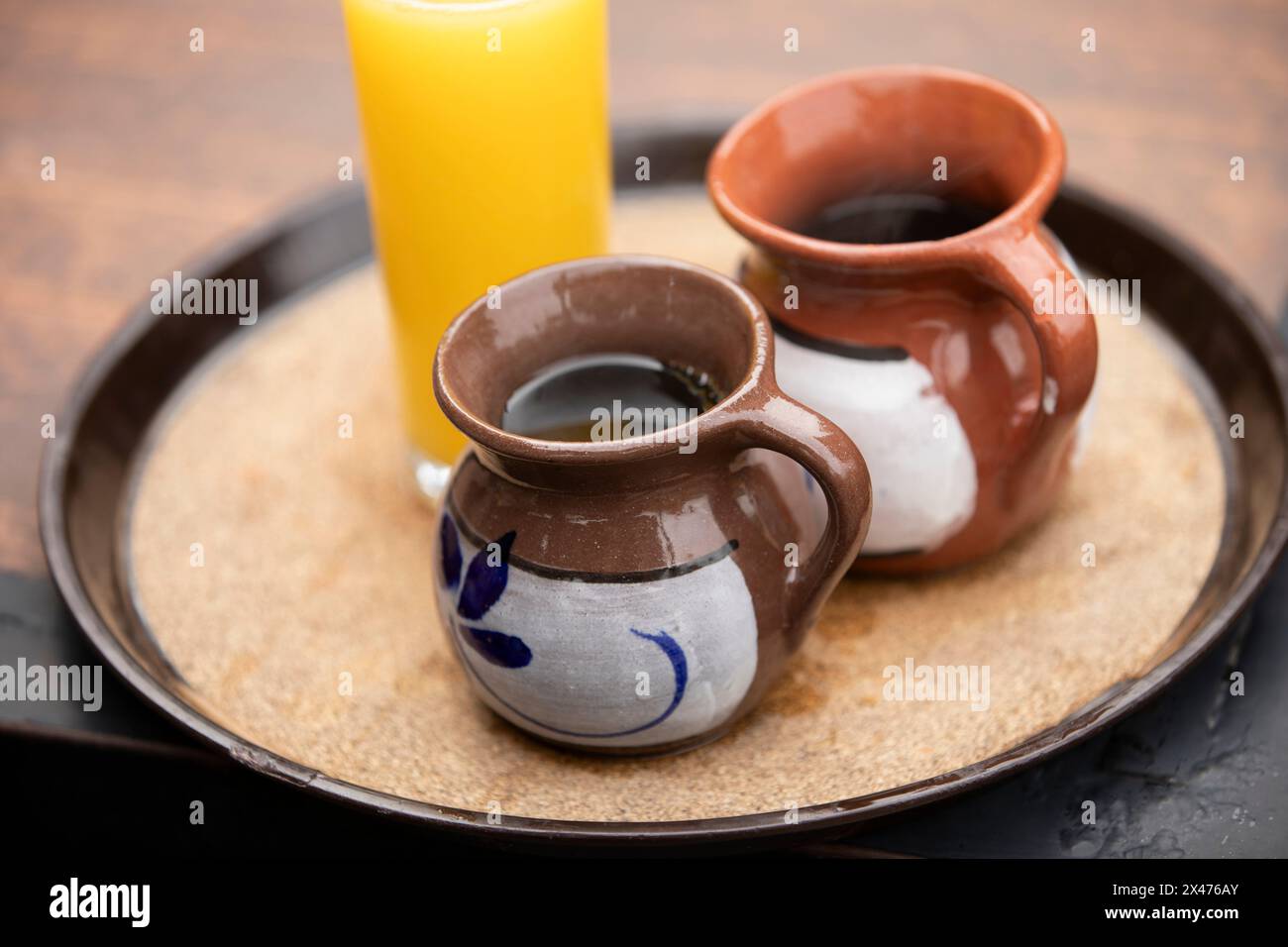 Due tazze di caffè messicano speciale, café de olla, servite in tazze di argilla insieme a un bicchiere di succo d'arancia su un vassoio a Bernal, Querétaro, Messico. Foto Stock Due tazze di caffè messicano speciale, café de olla, servite in tazze di argilla insieme a un bicchiere di succo d'arancia su un vassoio a Bernal, Querétaro, Messico. Foto Stock