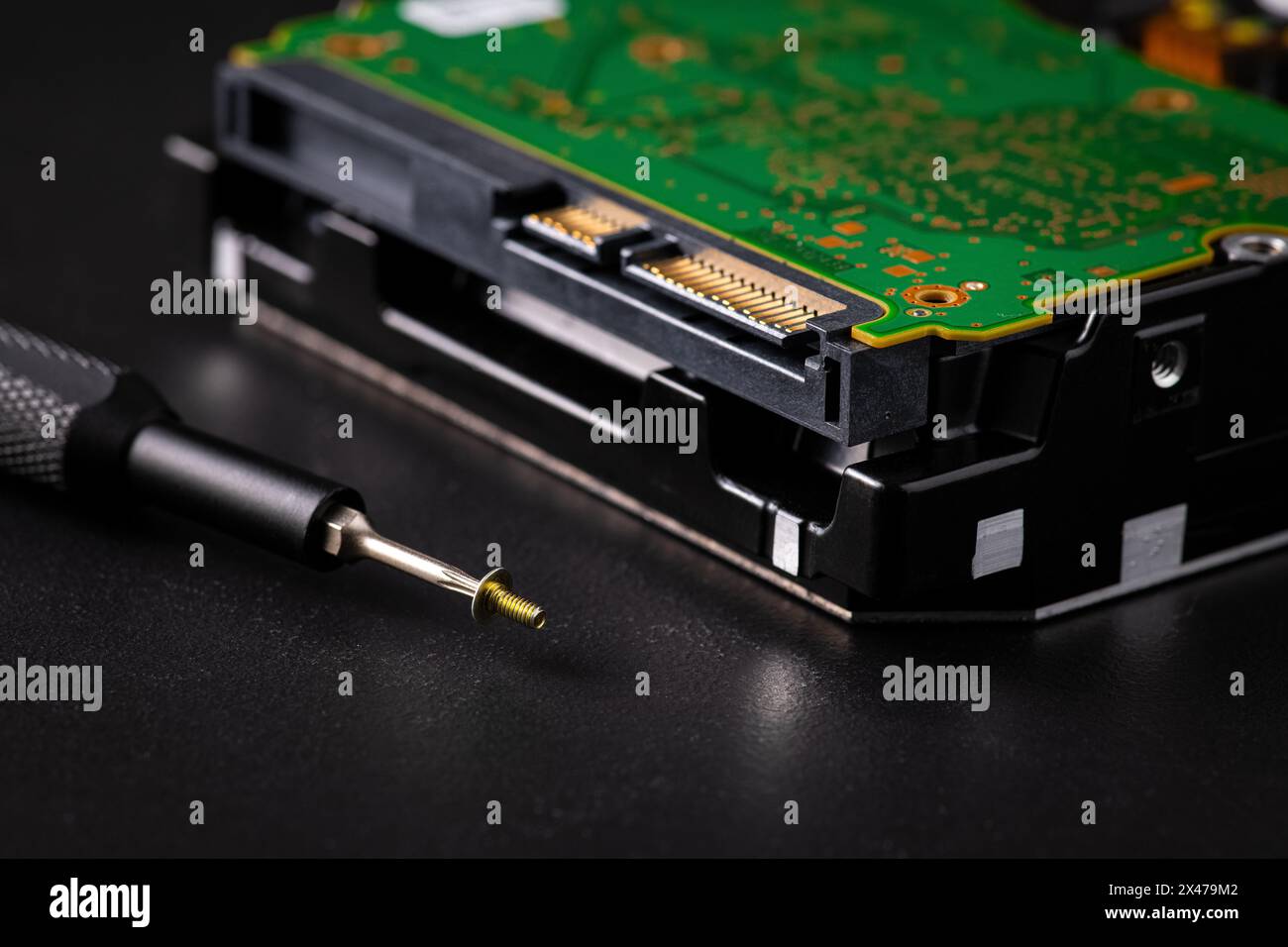 Unità disco rigido e scheda a circuito stampato con connettore di alimentazione SATA. Punta Torx con cacciavite magnetico e piccola vite a macchina su sfondo scuro. Foto Stock