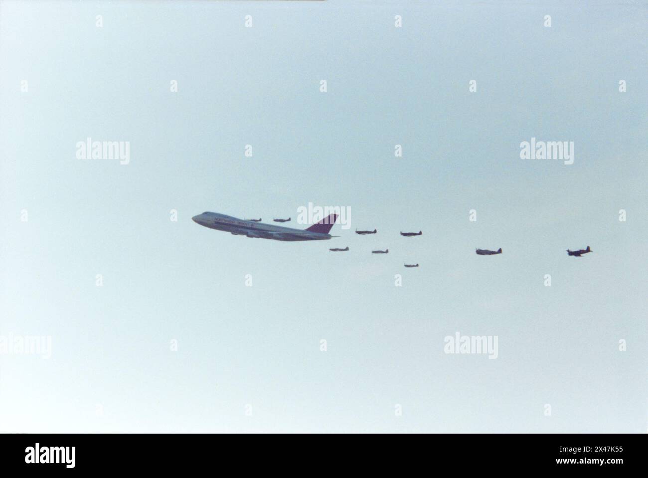 Northwest Orient Airlines Boeing 747 Jumbo Jet in volo in formazione con un gruppo di aerei da caccia della seconda guerra mondiale durante il North Weald Fighter Meet Airshow nel 1986. Un evento unico organizzato per celebrare il 60° anniversario della Northwest Orient Airlines. Gli aerei da combattimento della seconda guerra mondiale includevano uno Spitfire, Mustang, Thunderbolt e Corsair Foto Stock