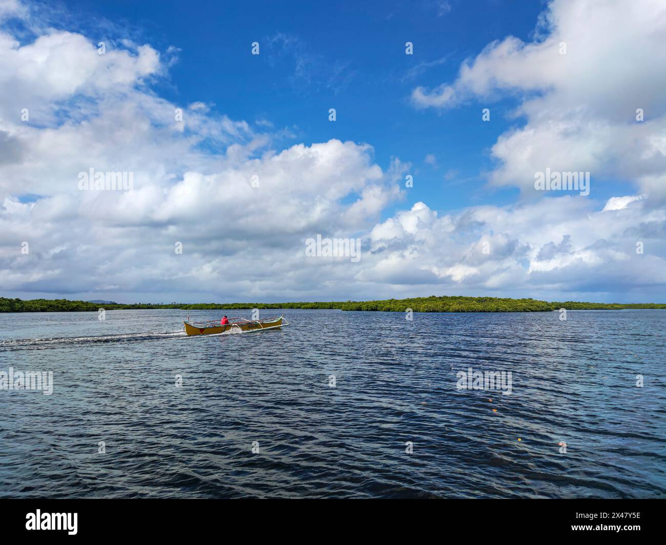 Un uomo pilota una barca a motore in mezzo a un paesaggio surreale di nuvole e foreste di mangrovie. Foto Stock
