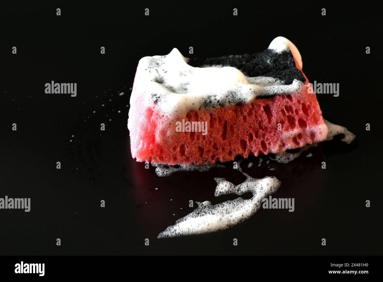 Su uno sfondo nero è presente una spugna con schiuma di sapone bianca. Foto Stock