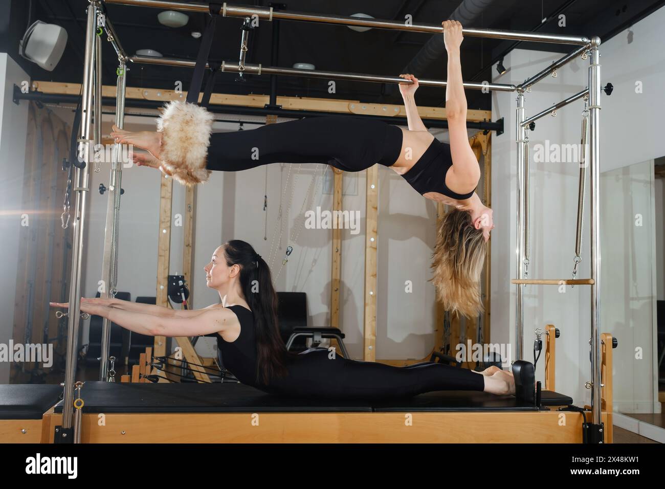 Due donne praticano esercizi di fitness fisico su una macchina Pilates in una stanza con pavimento in legno duro. I loro movimenti mostrano una bella balanc Foto Stock