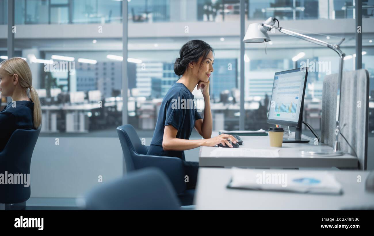 In Big Corporate Office: Beautiful Asian Business Manager che utilizza computer, uomini d'affari ed esperti che lavorano intorno a lei, analisi di statistiche, dati commerciali, piani di marketing. Foto Stock