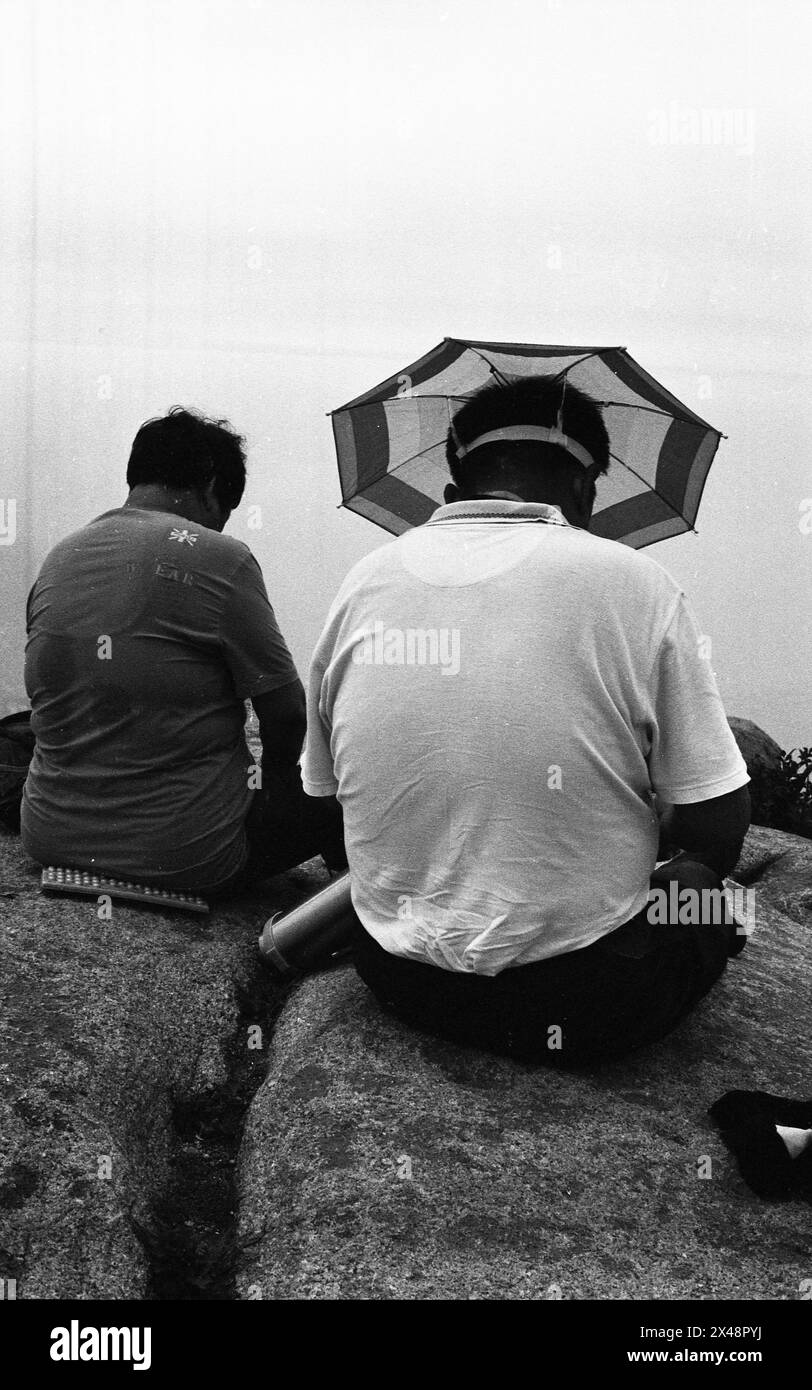 Nell'estate del 2014, in cima al monte Lao a Qingdao, nella provincia di Shandong, si potevano vedere una coppia da dietro, seduti vicino insieme su una cima rocciosa. Uno degli uomini aveva un ombrello sopra la testa, nonostante il tempo fosse coperto dal sole. /Cina Foto Stock