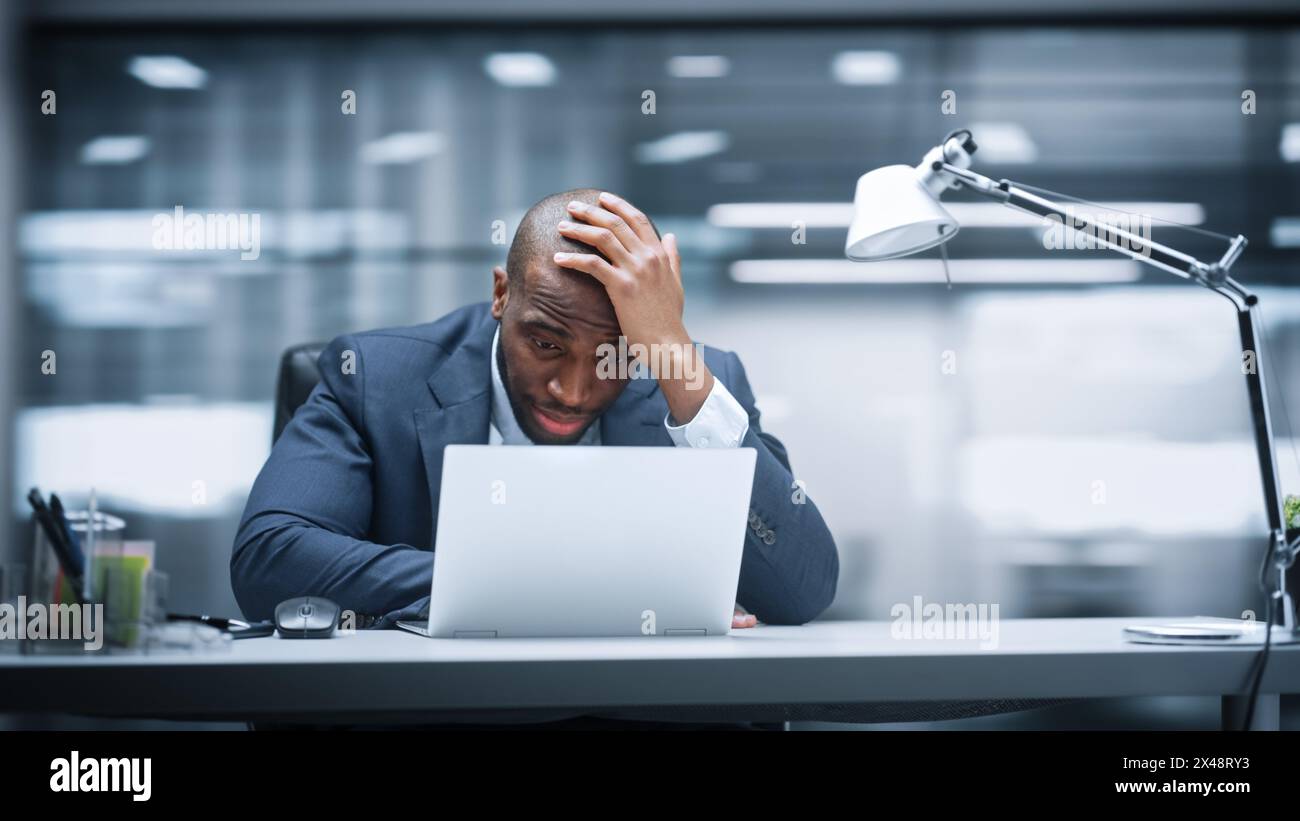 Ufficio moderno: Un uomo d'affari seduto alla scrivania lavora su un notebook, perde in borsa reagisce emotivamente, deluso. L'imprenditore d'affari in una tuta soffre di un brutto crollo del mercato. Sfondo sfocatura movimento Foto Stock