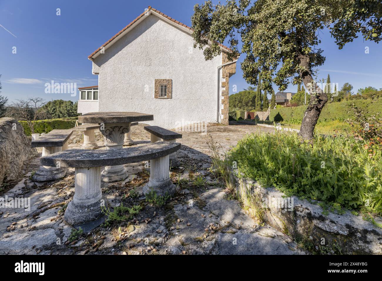 Una casa di campagna con facciate bianche, pavimenti in pietra sul terreno e un tavolo con panchine di cemento Foto Stock
