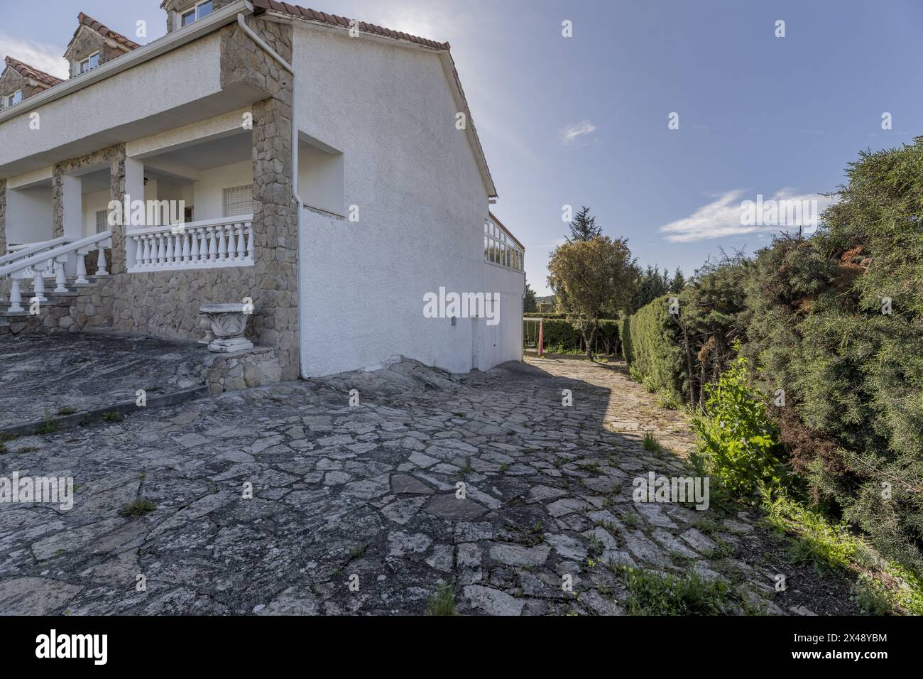 Una casa di campagna con facciate bianche, pavimenti in pietra sul terreno e siepi perimetrali Foto Stock