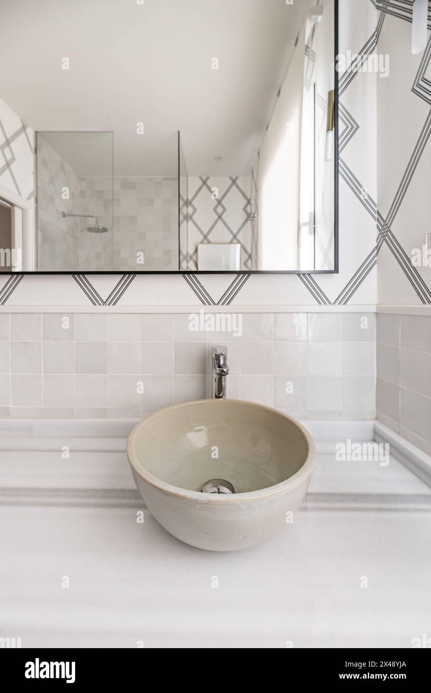 Bagno con lavabo singolo, non incorporato nel ripiano in marmo, carta decorativa sulla parete e specchio con bordo in metallo nero Foto Stock