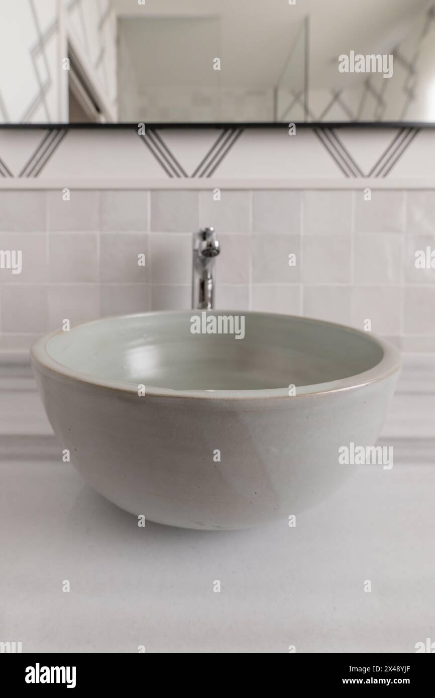 Bagno con lavabo a una ciotola di mezza circonferenza in terracotta cotta cotta cotta, non incastonato in un ripiano in marmo, carta decorativa sulla parete e un mirro Foto Stock