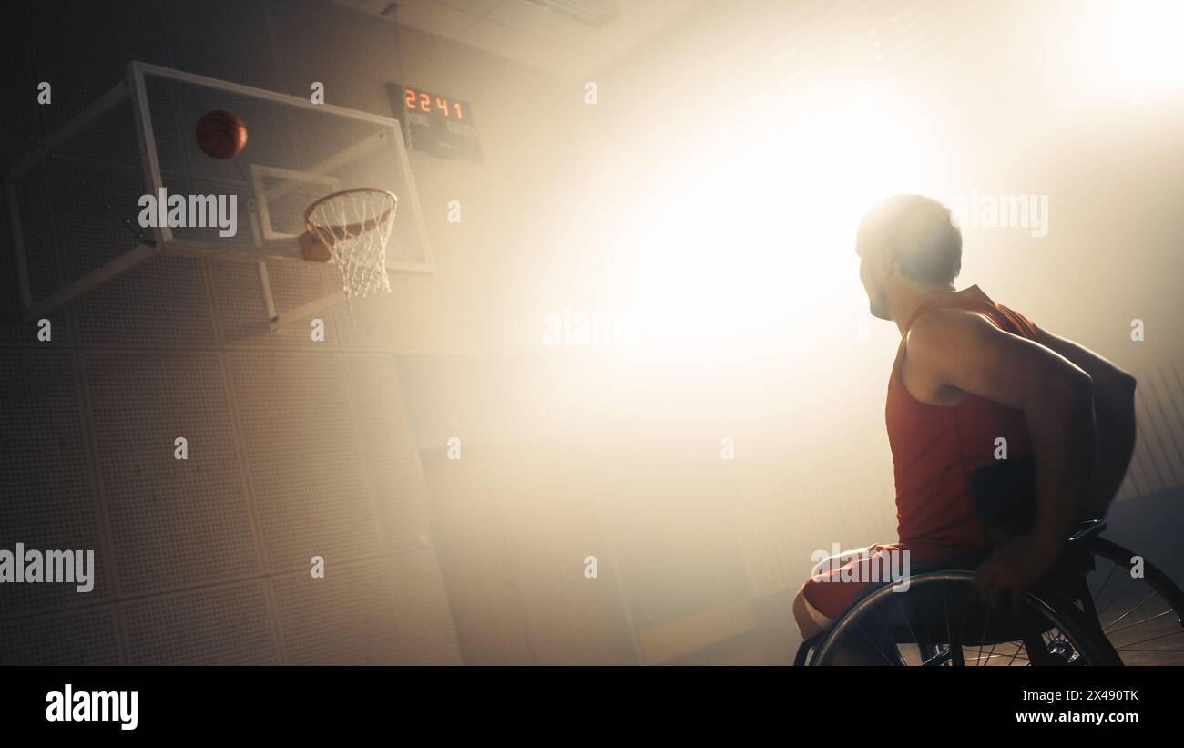 Giocatore di pallacanestro in sedia a rotelle che indossa la palla da tiro in uniforme rossa con successo, segnando un gol perfetto. Determinazione, ispirazione di una persona con disabilità. Angolo olandese con colori caldi e nebbiosi Foto Stock