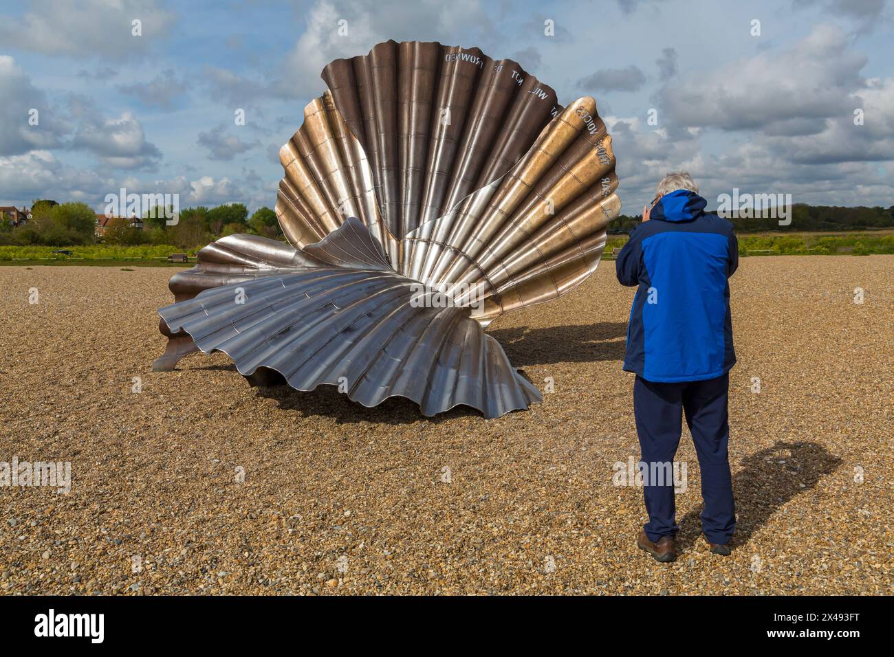 Uomo che scatta foto della scultura di Scallop sulla spiaggia di Aldeburgh, Suffolk, Regno Unito ad aprile Foto Stock