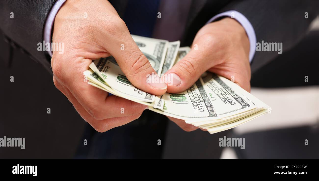 Uomo in tuta e cravatta tenere in braccio pack di centinaia di fatture del dollaro closeup. Mercato stock exchange guadagnare pila ricco dono attuale datore di lavoro servizio di pagamento anticipato gr Foto Stock