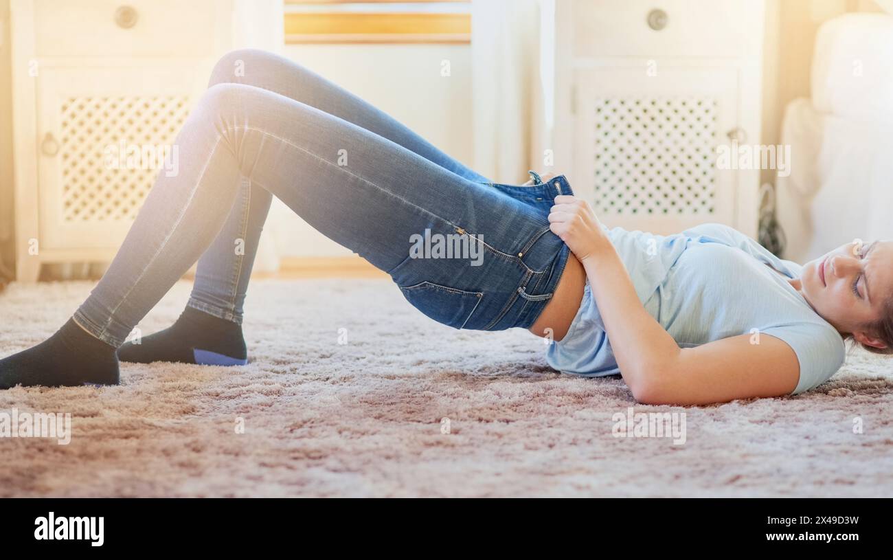Donna, casa e lotta con i jeans sul pavimento per vestirsi, aumentare di peso, forza e strette. Luce soffusa, persona femminile e camera da letto con sdraiato sul pavimento Foto Stock