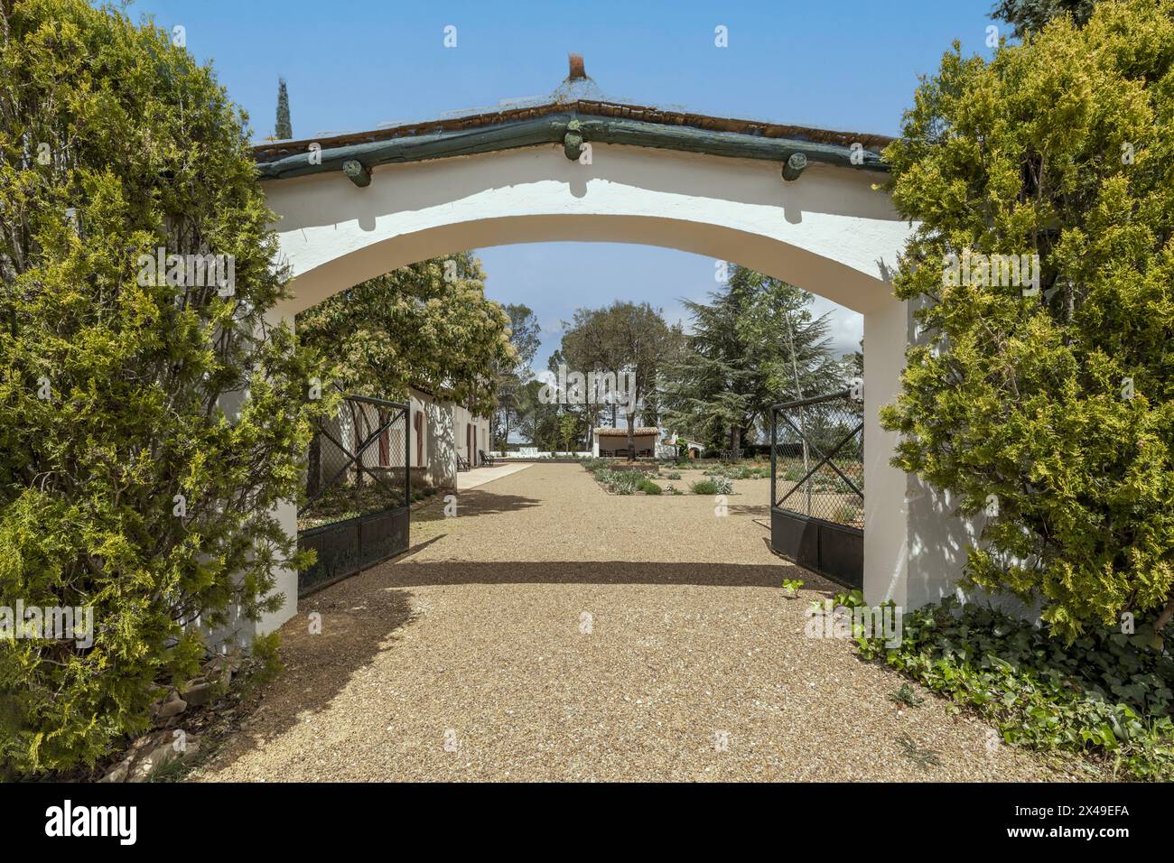 Arco d'ingresso nel recinto perimetrale di una casa di campagna in stile andaluso con pareti bianche, sentieri di ghiaia e una grande varietà di alberi Foto Stock