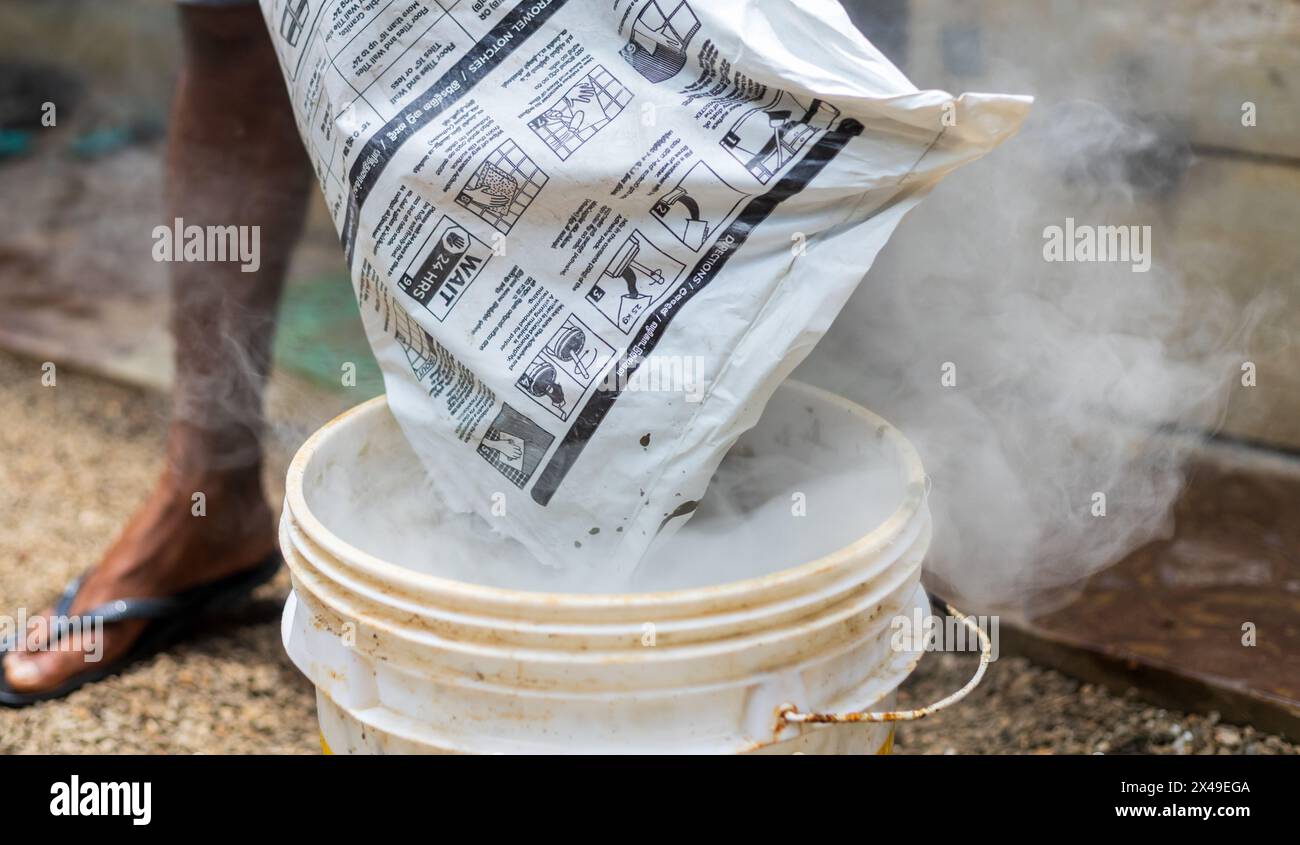 versare cemento per intonacare in un secchio per mescolare e preparare una pasta. condizioni di lavoro non sicure. Foto Stock