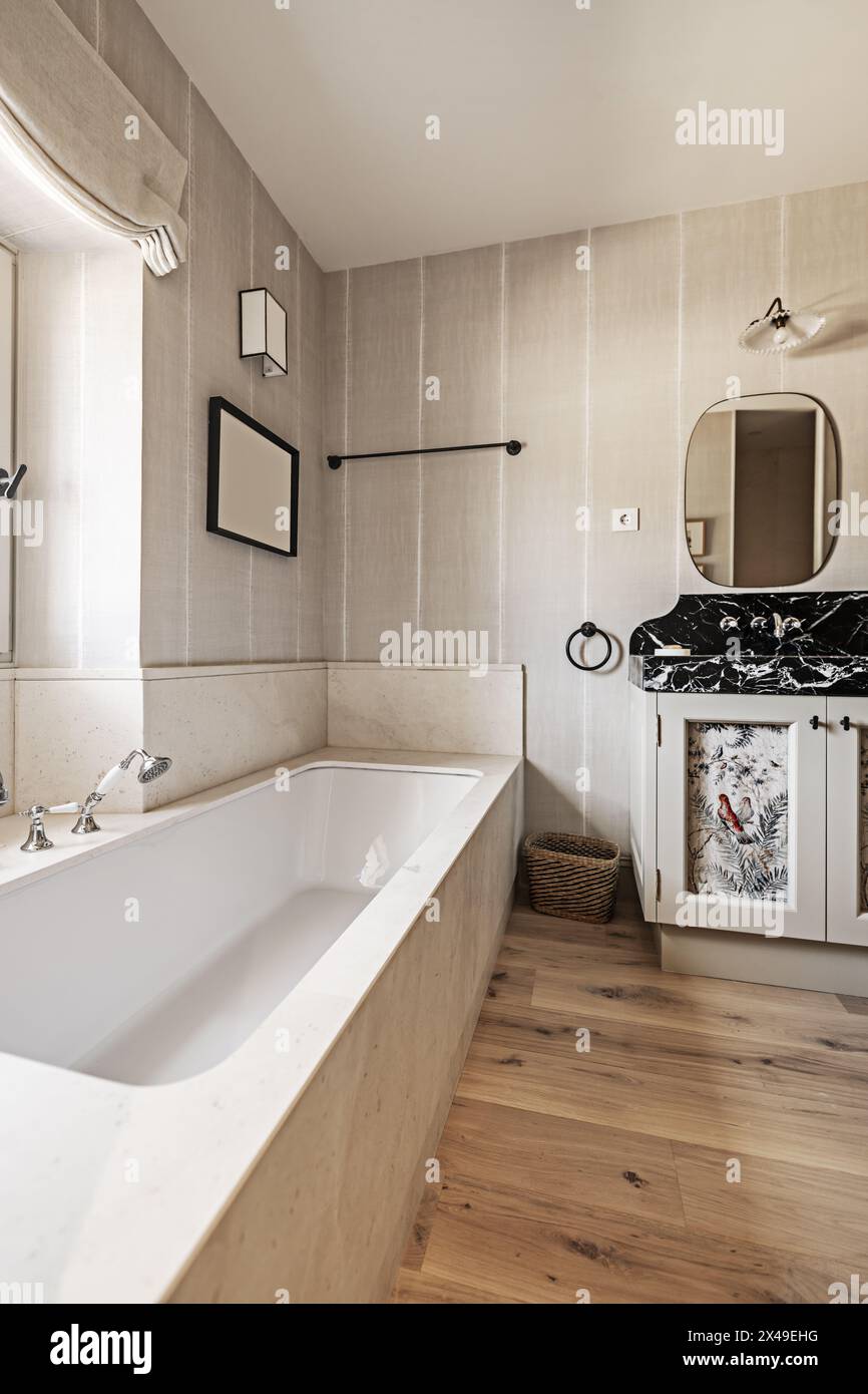Una vasca da bagno in porcellana bianca con cornici in marmo con rubinetti in stile vintage e un armadietto con un ripiano in marmo nero e specchi alle pareti Foto Stock