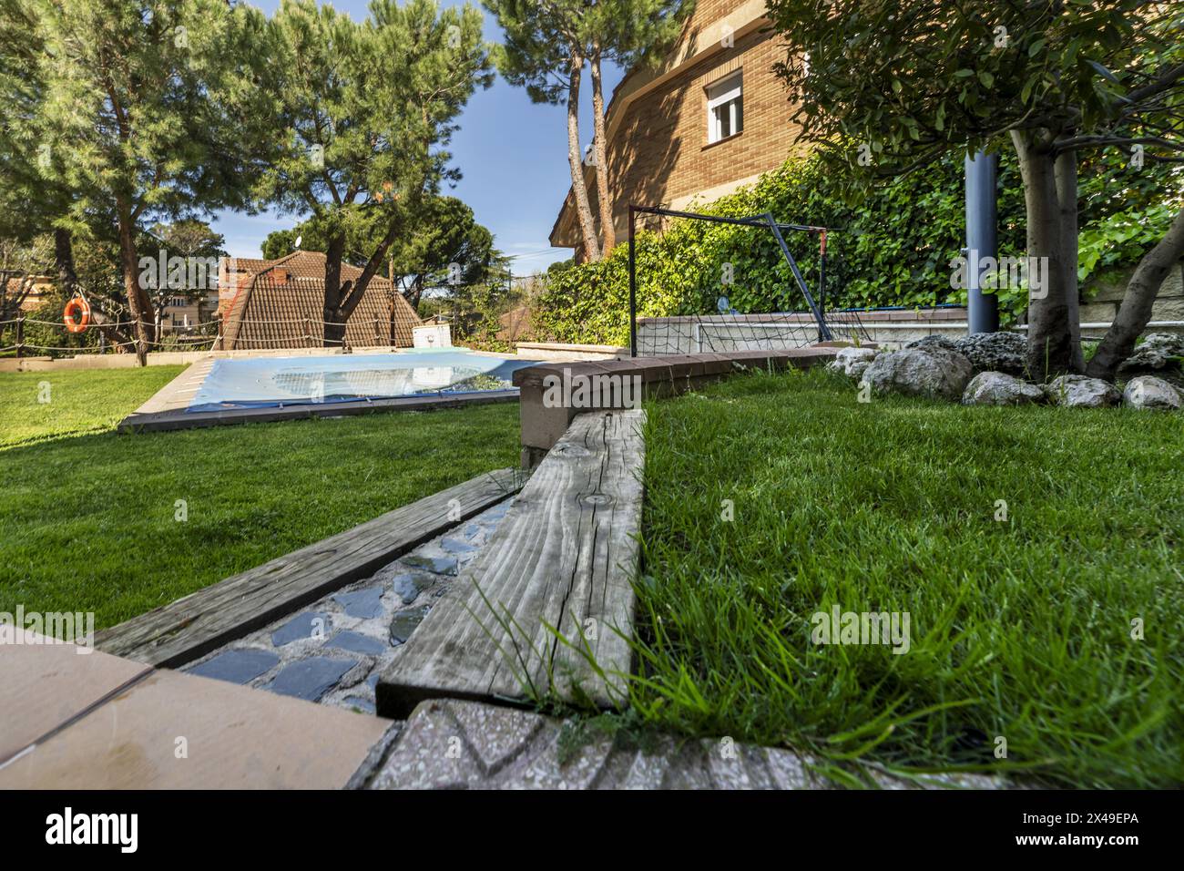 giardino con sentiero piastrellato che conduce ad una piscina con traversine in legno e pavimenti in erba naturale Foto Stock