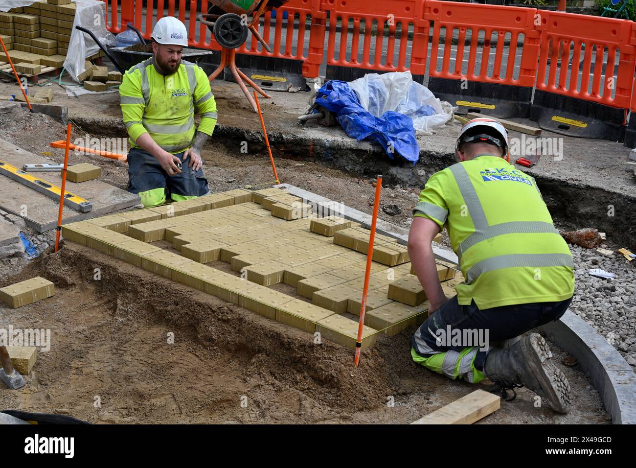 Il lavoratore posa delle lastre di pavimentazione tattili per l'attraversamento di strade pedonali per assistere i non vedenti Foto Stock