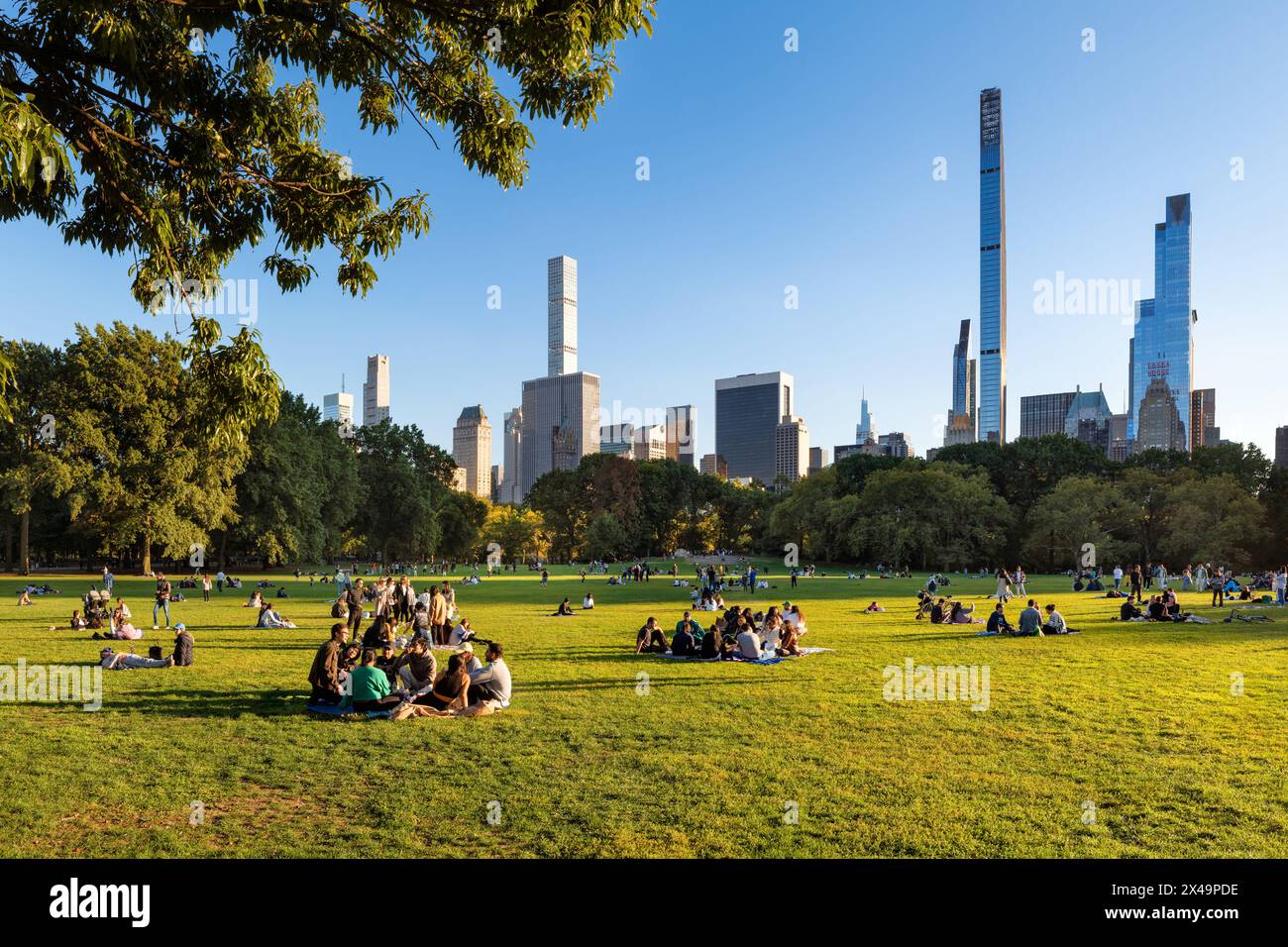 New York City Central Park Sheep Meadow nel tardo pomeriggio estivo con persone che si rilassano sull'erba al sole. Vista sui grattacieli di Billionaires'Row Foto Stock