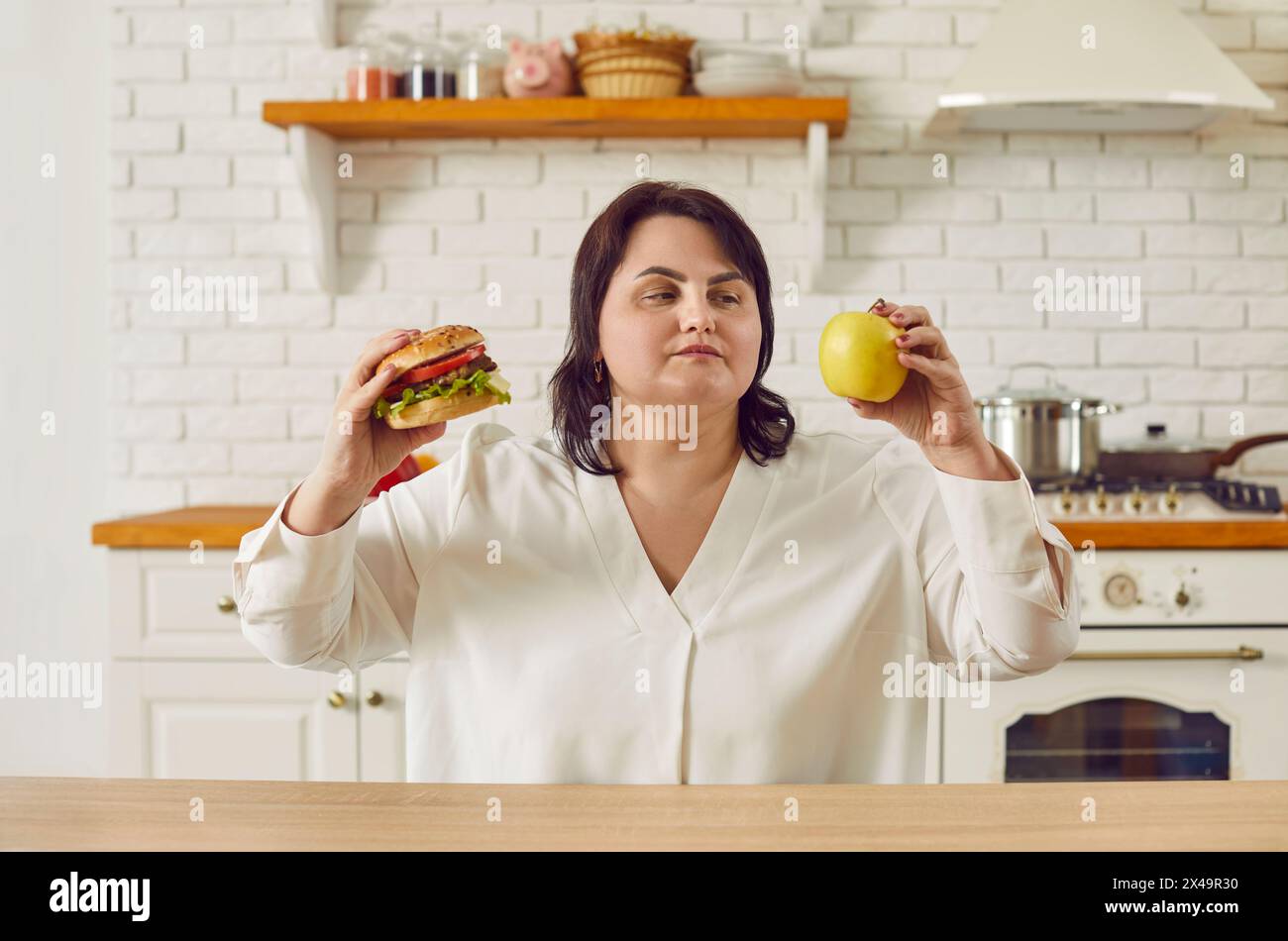 Sovrappeso, donna bruna grintosa che sceglie tra mangiare sano e malsano Foto Stock