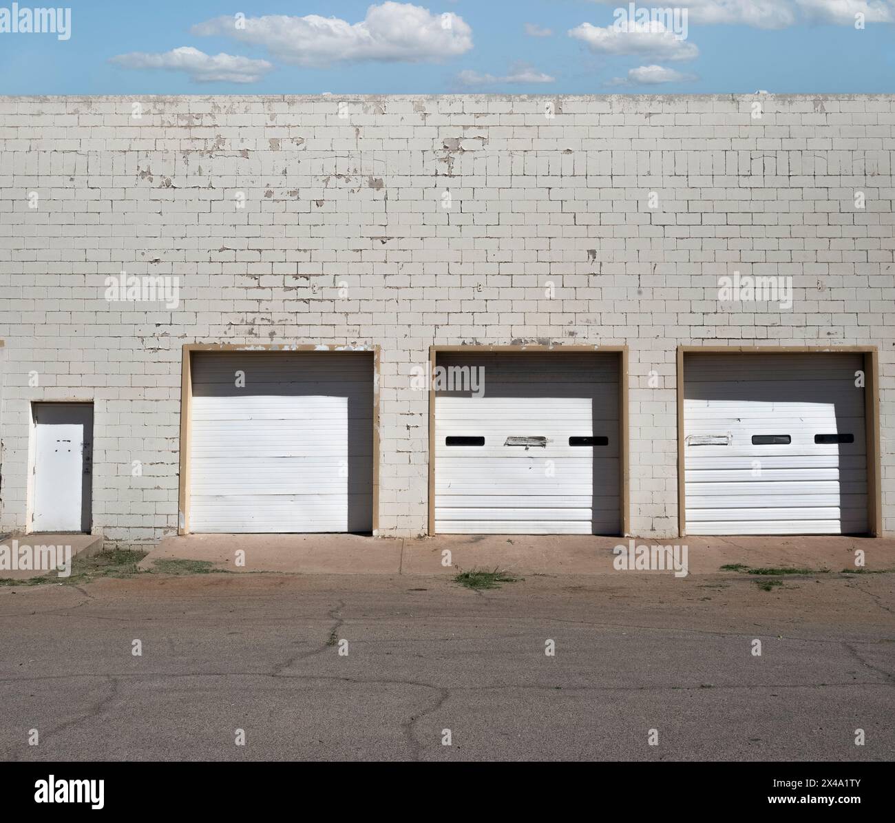 trascurato e datato ma funzionale decadimento urbano commerciale con atmosfera di metà secolo, tre porte bianche del garage in un edificio in mattoni bianchi con porta Foto Stock