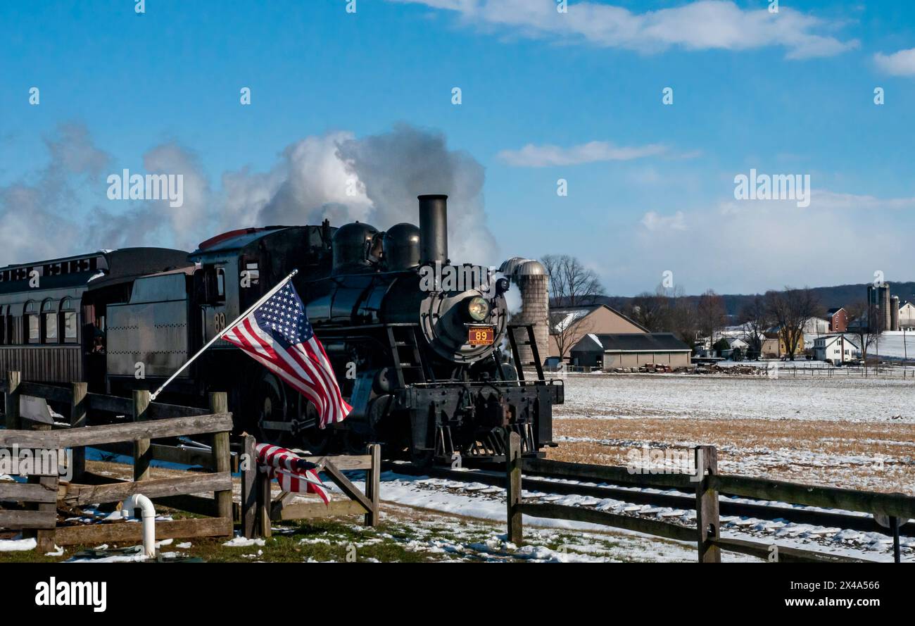 Ronks, Pennsylvania, USA, 17 febbraio 2024 - Un treno a vapore sta tirando un vagone con una bandiera americana. Il treno sta viaggiando attraverso una neve Foto Stock Ronks, Pennsylvania, USA, 17 febbraio 2024 - Un treno a vapore sta tirando un vagone con una bandiera americana. Il treno sta viaggiando attraverso una neve Foto Stock