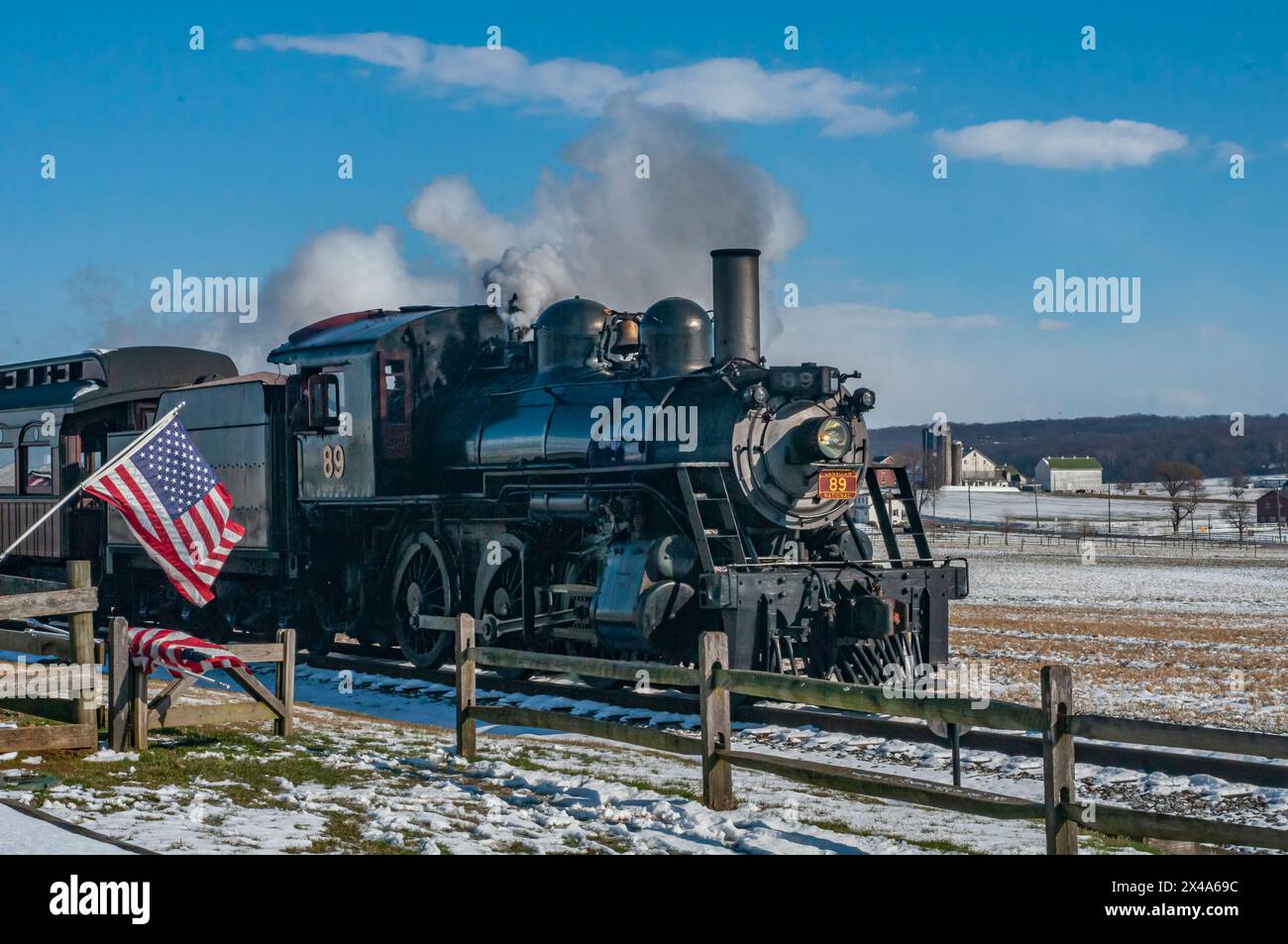 Ronks, Pennsylvania, USA, 17 febbraio 2024 - Un treno a vapore sta tirando un vagone con una bandiera americana. Il treno sta viaggiando attraverso una neve Foto Stock Ronks, Pennsylvania, USA, 17 febbraio 2024 - Un treno a vapore sta tirando un vagone con una bandiera americana. Il treno sta viaggiando attraverso una neve Foto Stock