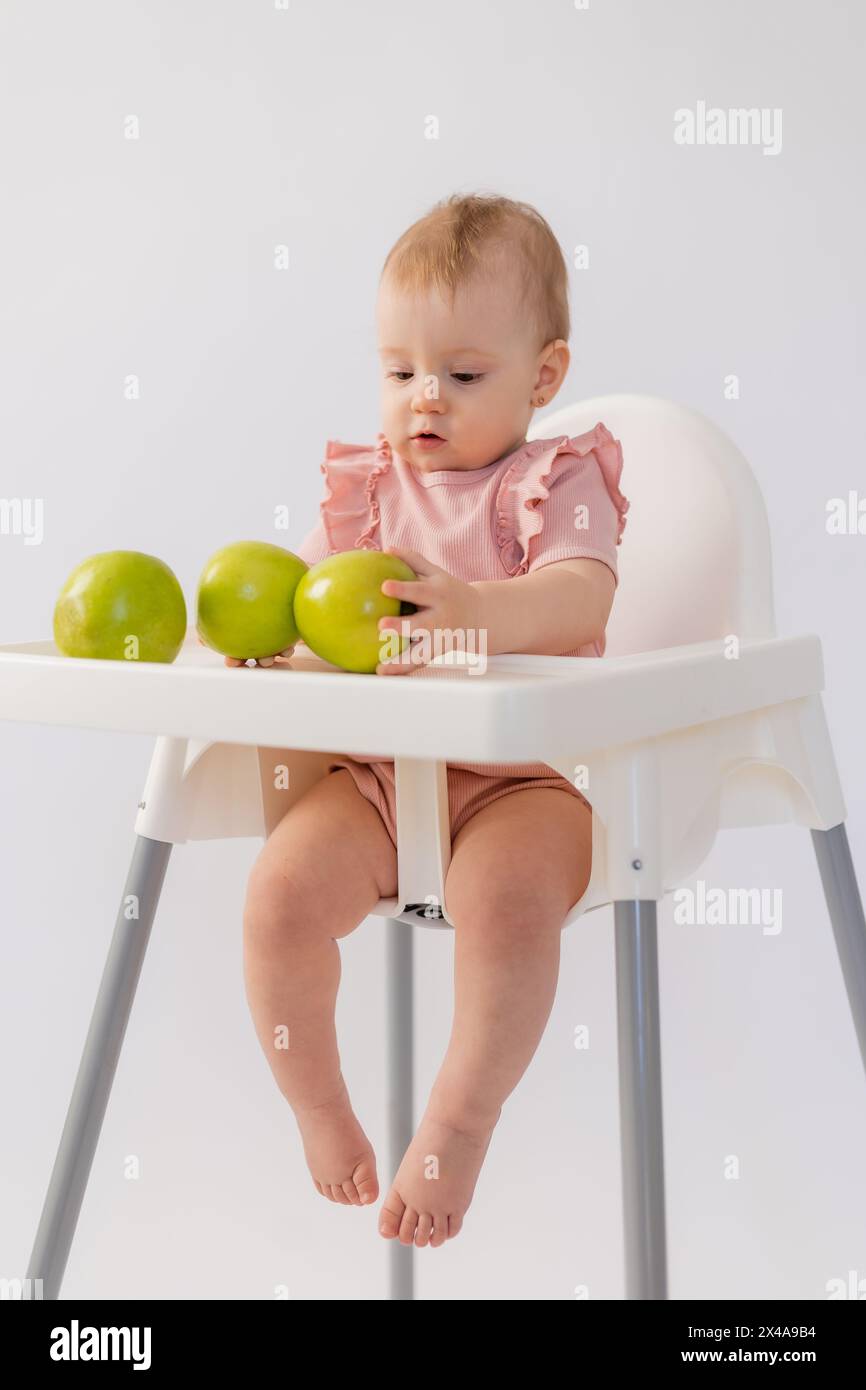 Un bambino carino in una sedia per bambini stuzzica le mele su sfondo bianco. Foto di alta qualità Foto Stock