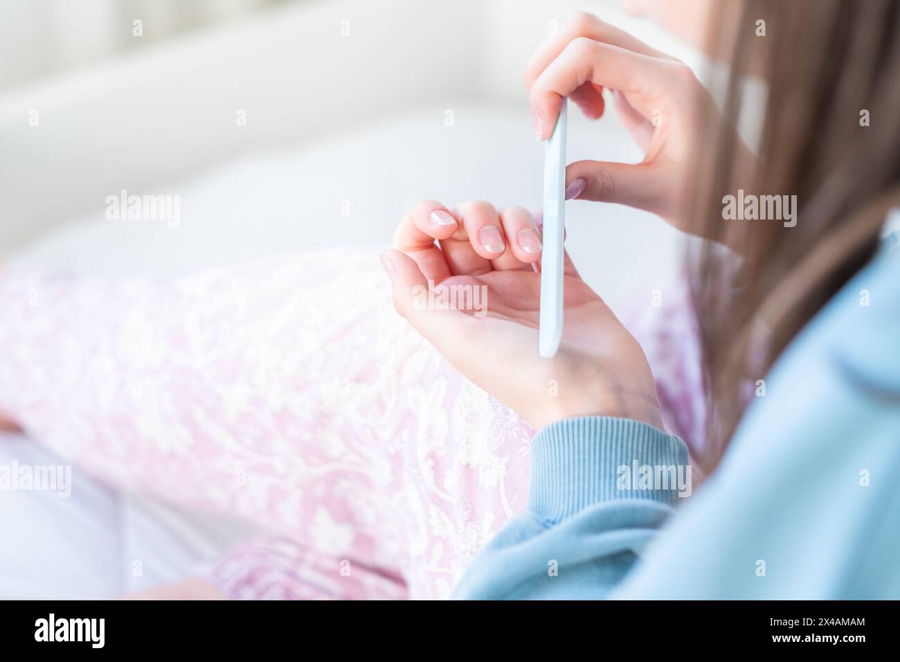 Una giovane adolescente si afferra le unghie in modo rilassato mentre si siede sul letto. Ha la mano arricciata per essere più precisa Foto Stock