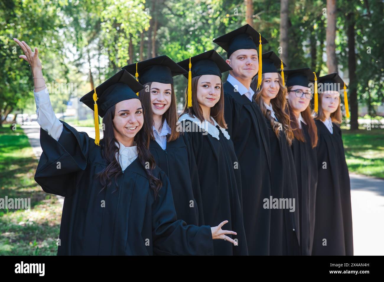 Fila di giovani felici in abiti da laurea all'aperto. Studenti nel parco. Foto Stock