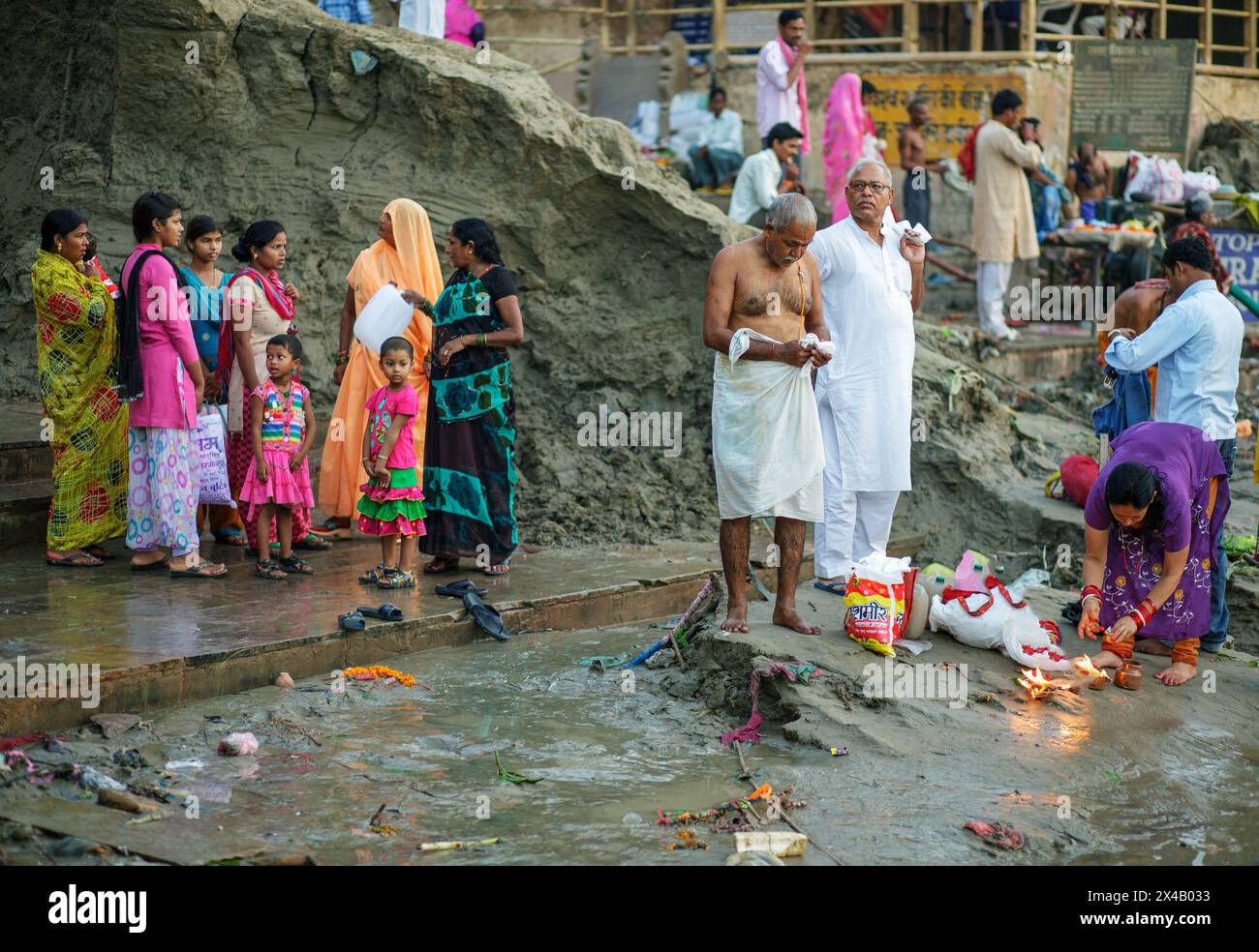 Pellegrini sulle rive del fiume Gange a Varanasi con alti mucchi di sedimenti alla fine della stagione dei monsoni. Foto Stock