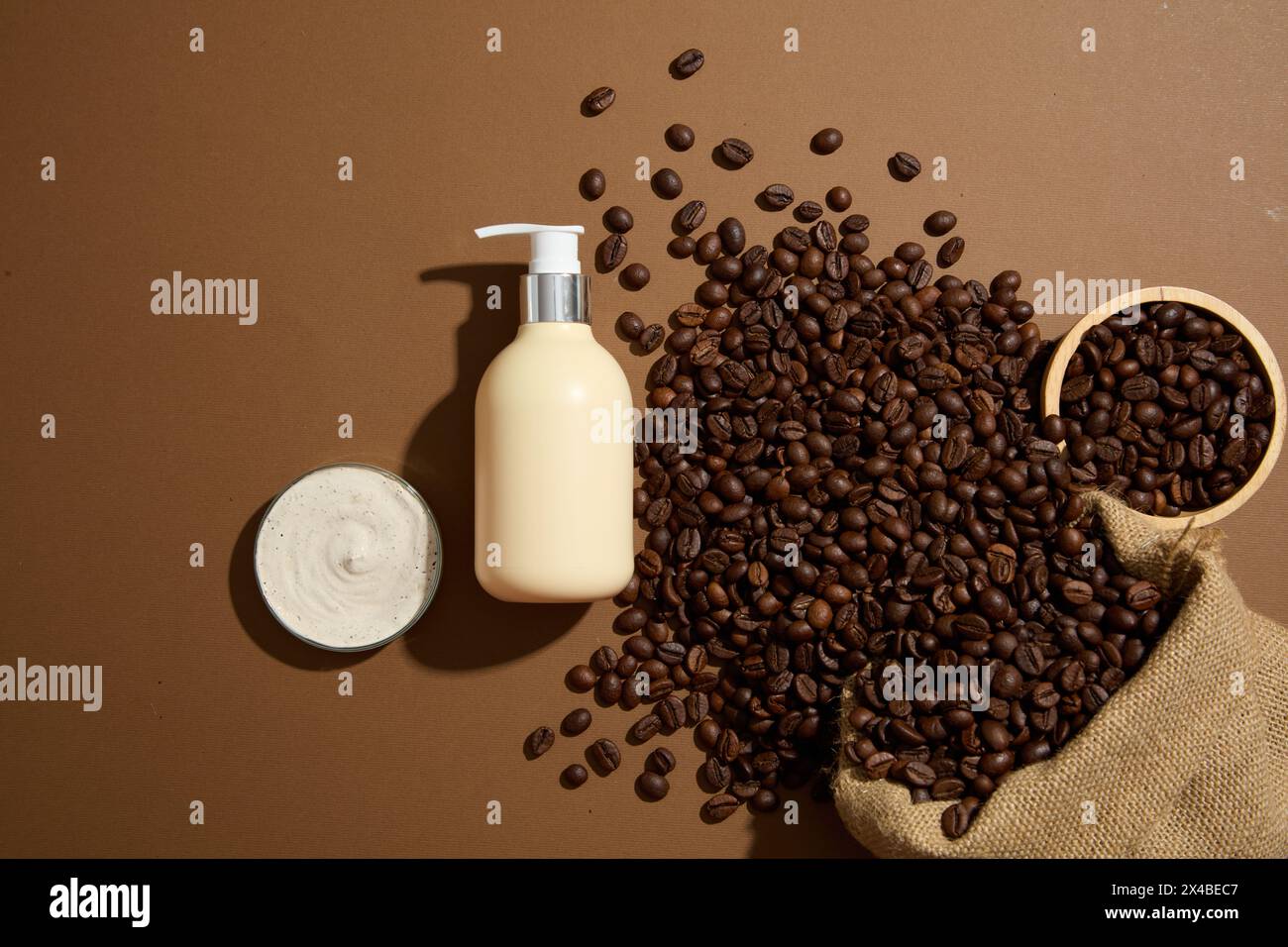 Una bottiglia cosmetica vuota posizionata su sfondo marrone con chicchi di caffè tostati marroni e consistenza panna. Scenografia minimalista per pubblicità e branding Foto Stock