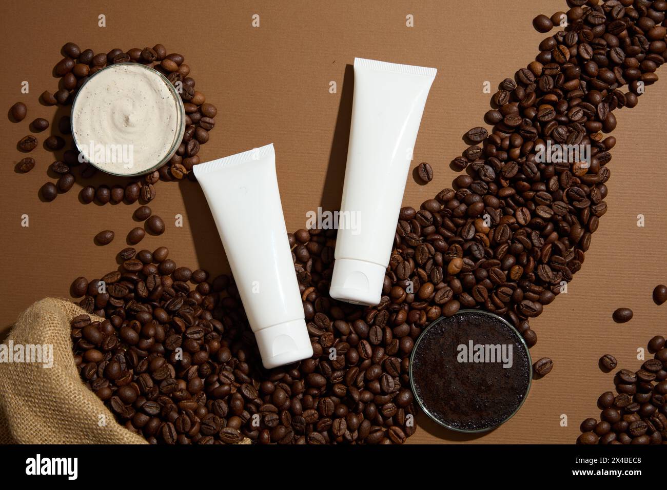 Scena minimalista per pubblicizzare cosmetici biologici con ingredienti naturali. Chicchi di caffè, polvere di caffè e consistenza panna su sfondo marrone con due condimenti Foto Stock