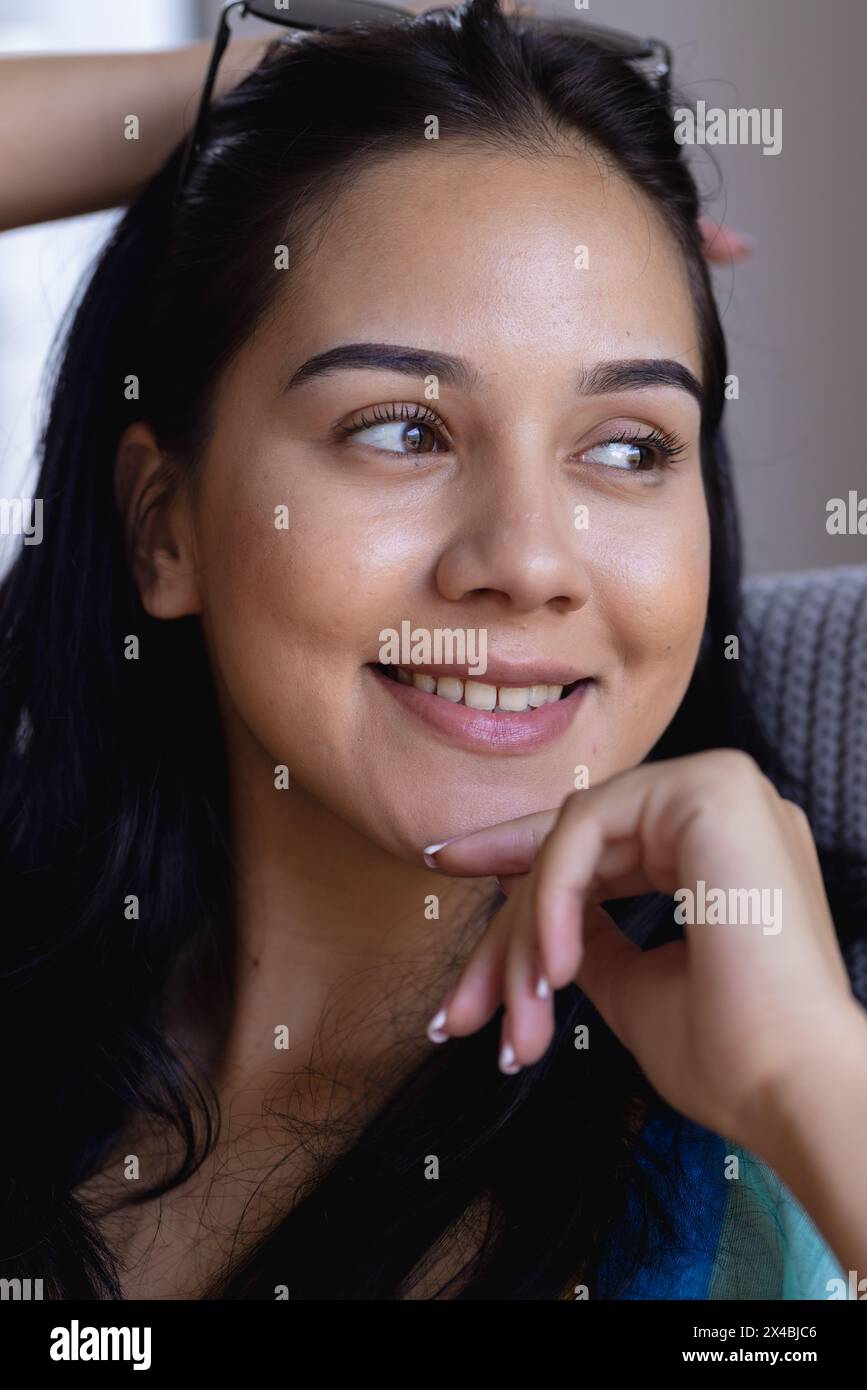 Giovane donna birazziale dal look premuroso, che riposa il mento a casa. Ha i capelli scuri, gli occhi marroni e la pelle limpida, con un trucco minimale, non alto Foto Stock