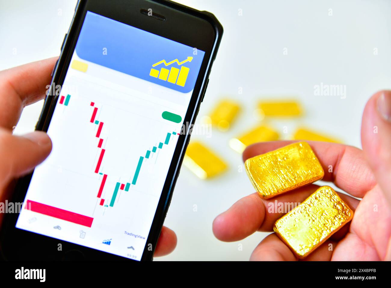 Tenere a mano uno smartphone e una barra d'oro per controllare il grafico del prezzo dell'oro per l'investimento Foto Stock