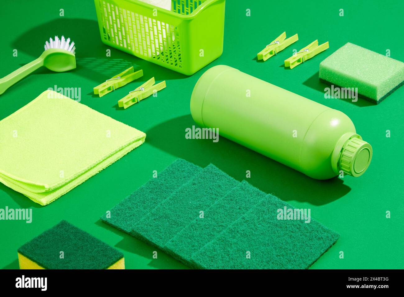 Prodotti per la pulizia verdi su sfondo verde semplice. Flacone di detergente, straccio, spazzola e spugne senza etichetta decorati. Concetto di pulizia della casa, scena per un Foto Stock