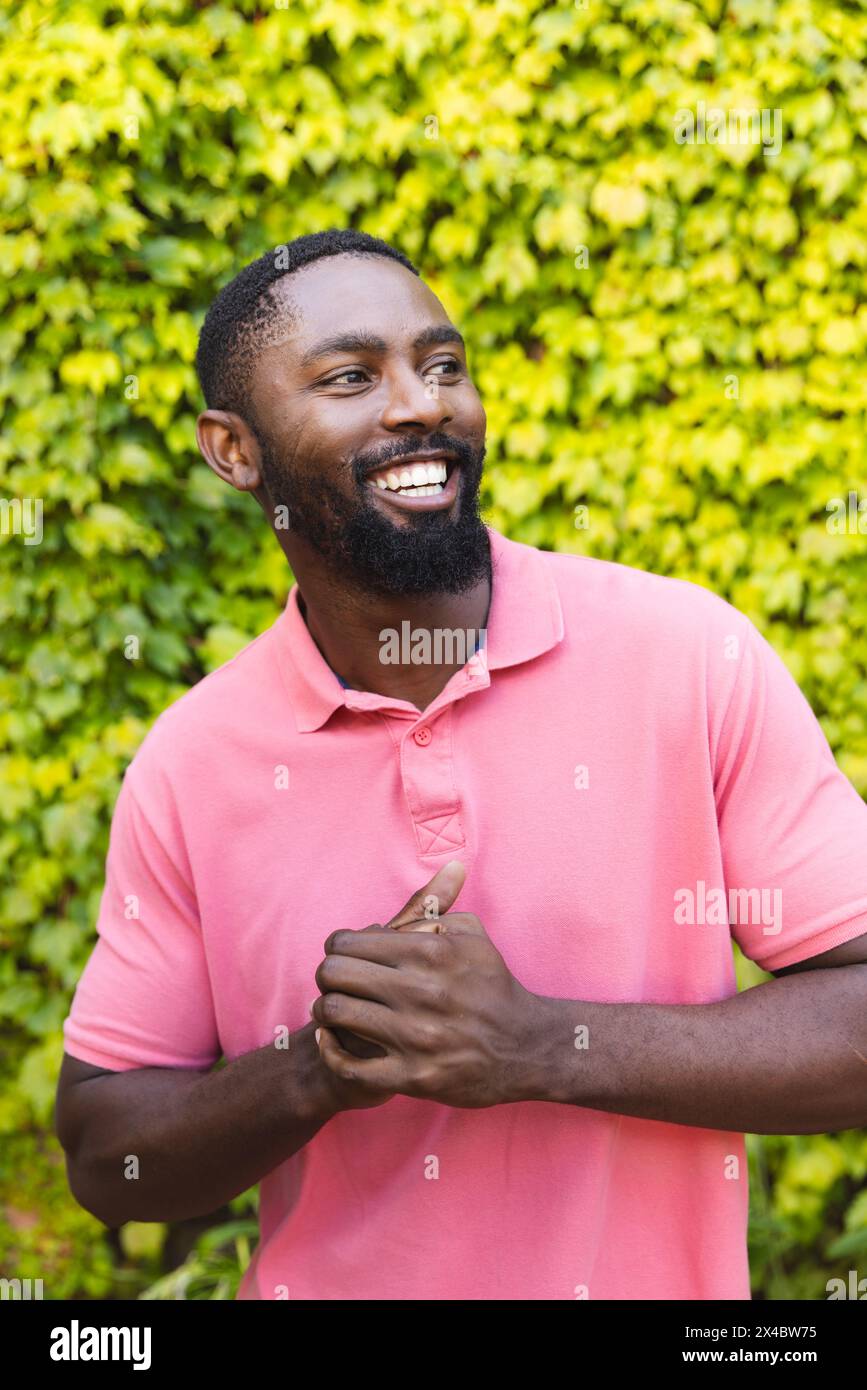 Uomo afroamericano che indossa una camicia rosa, ridendo all'aperto a casa. Ha la barba corta, i capelli neri corti e gli occhi scuri, inalterati Foto Stock